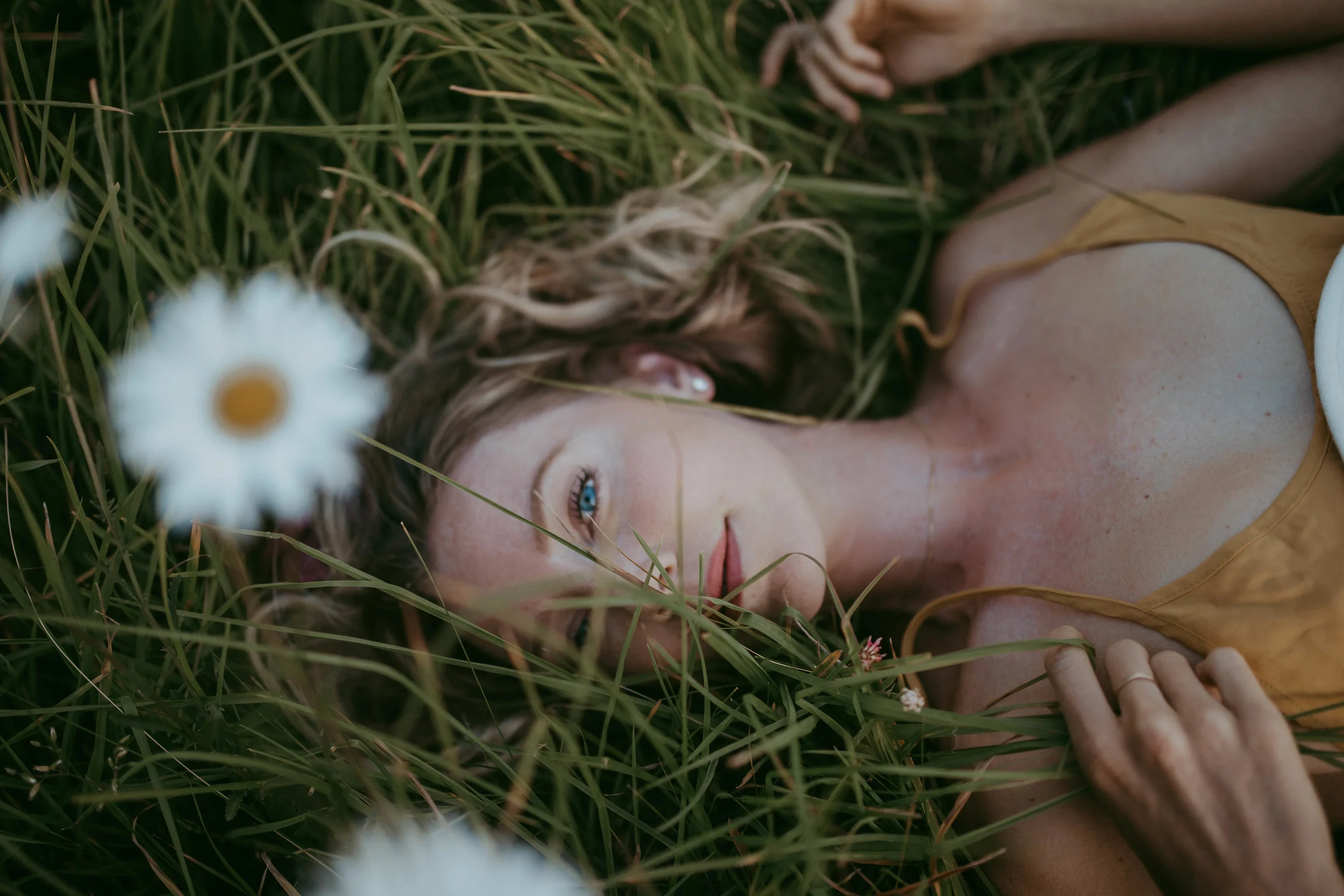 Woman lying in grass with daisies and wearing a yellow top.