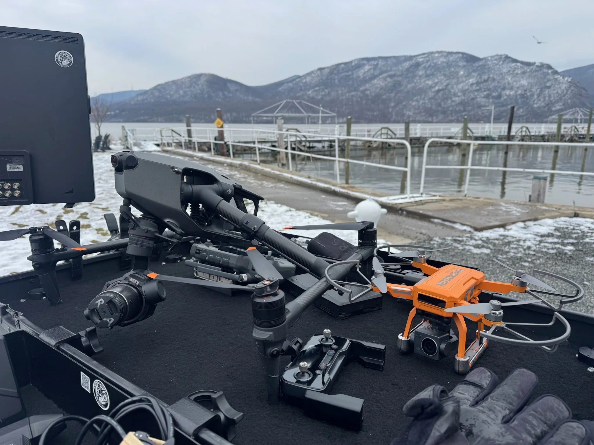 A drone on a boat near a snowy shoreline with mountains in the background.