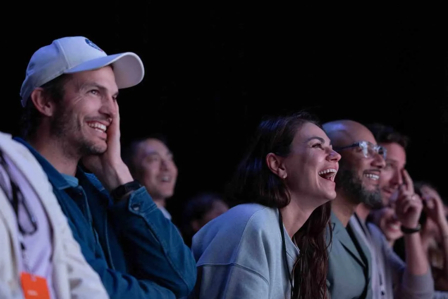 Ashton Kutcher and Mila Kunis laughing in the audience during a corporate event keynote in Los Angeles.
