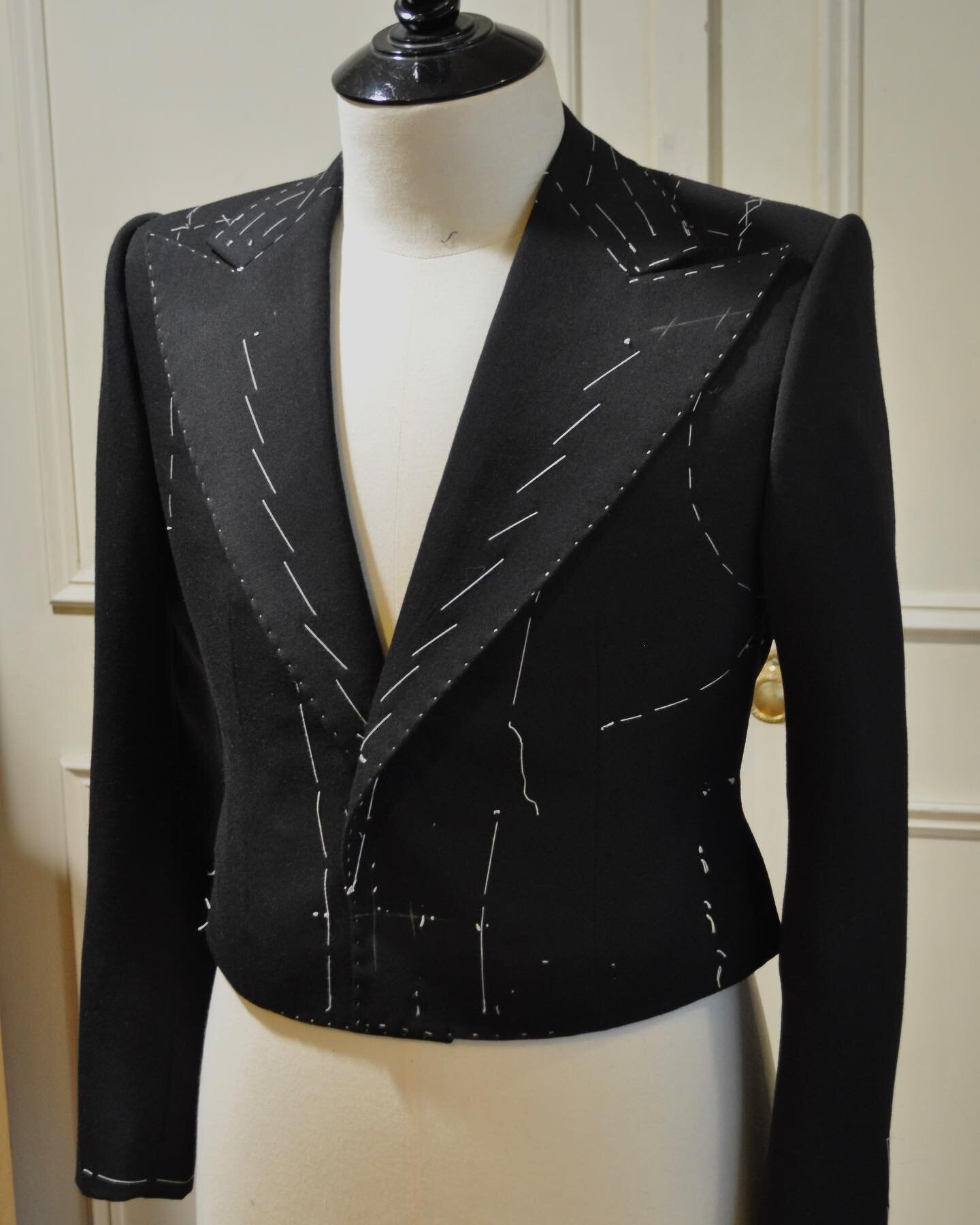 A mess style cropped jacket, in a black barathea ready to be finished . Cut with rounded seams to the back , and to be fastened with a link button .