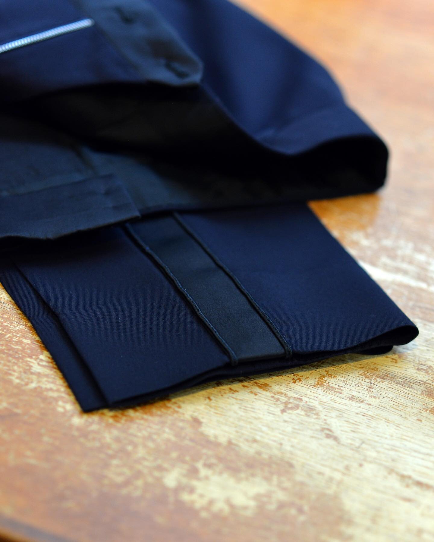 A handmade silk braid on the side of a pair of dress trousers . We make the braid in house by hand, painstakingly rolling silk satin into a strip, then sewing a narrow cord along each edge .