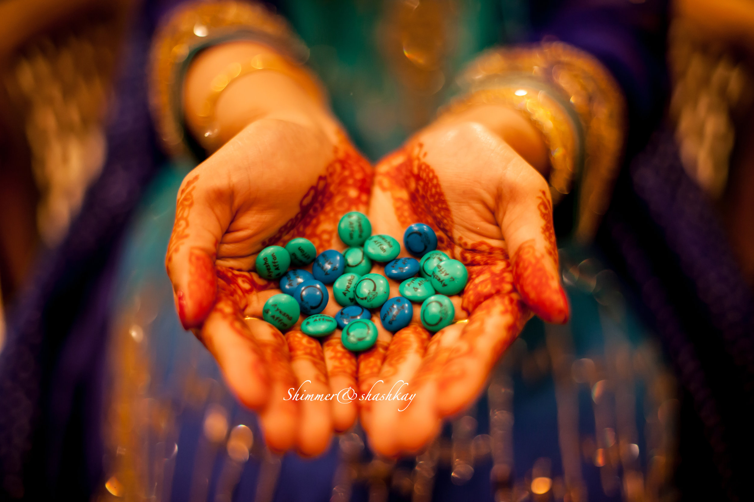 Hands decorated with henna holding blue and turquoise personalized M&M candies.