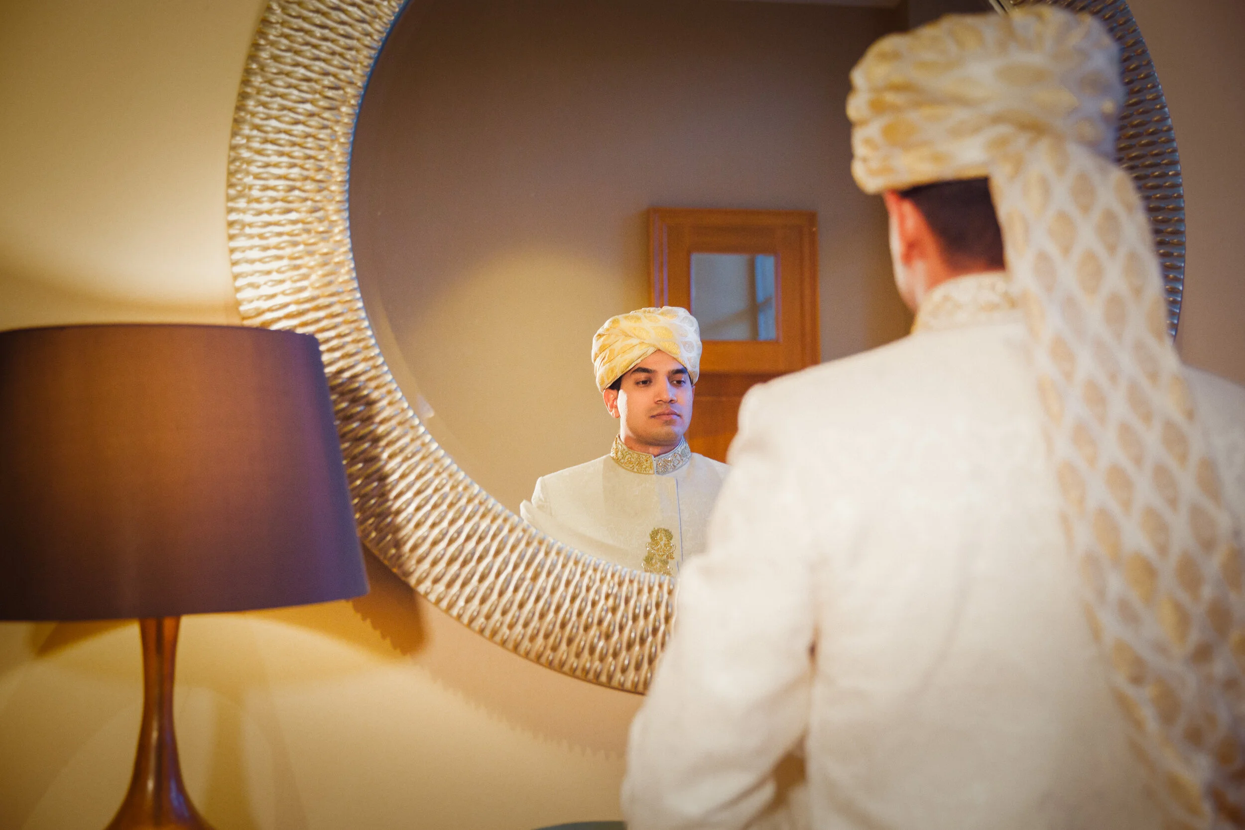 Man in traditional attire looking in a round mirror.