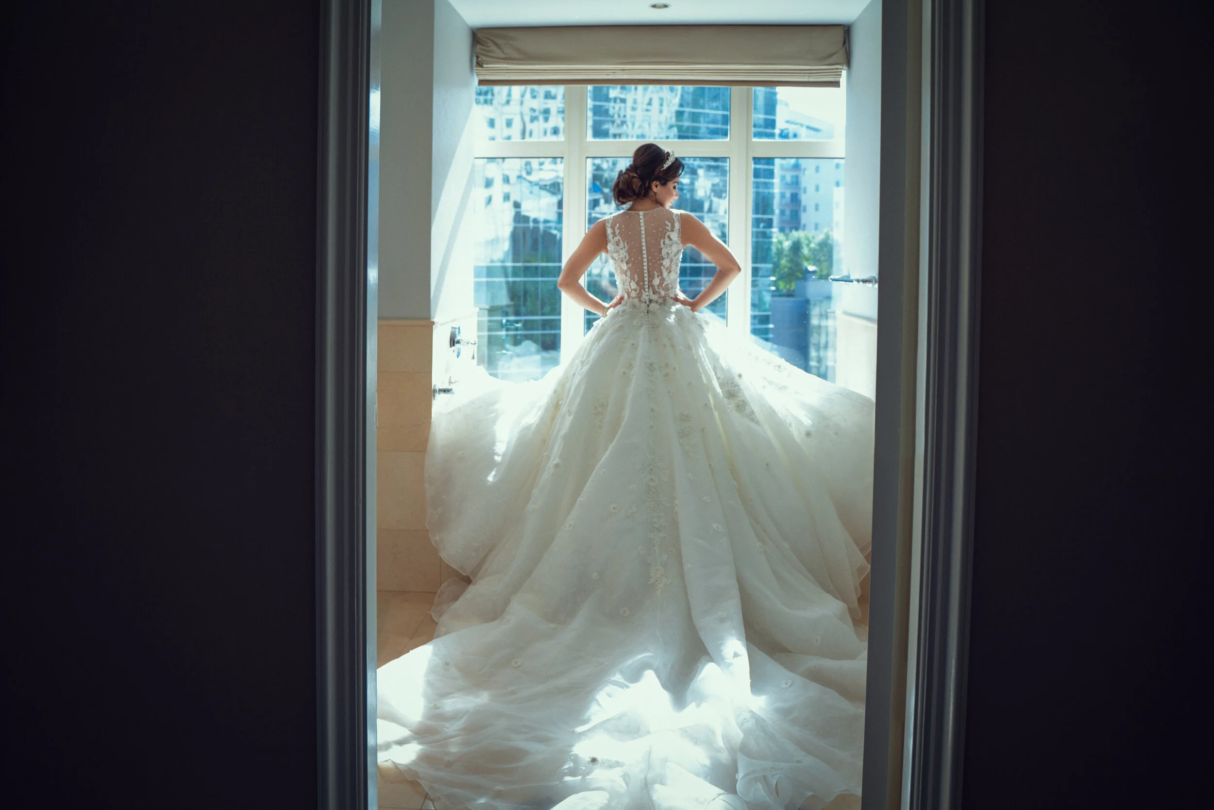 Bride in a white wedding dress standing in front of a large window.