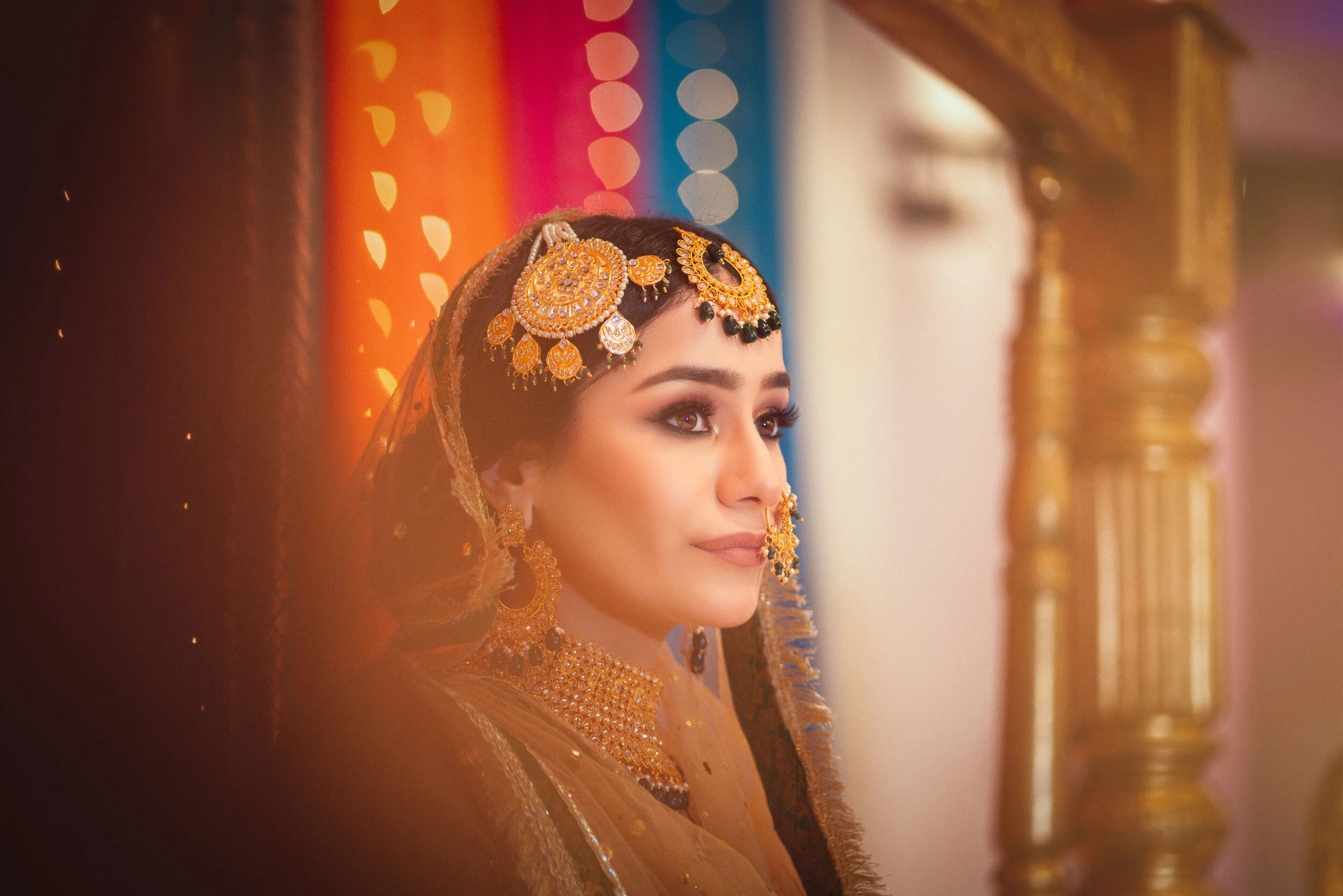 Woman in traditional bridal attire with golden jewelry, colorful background.