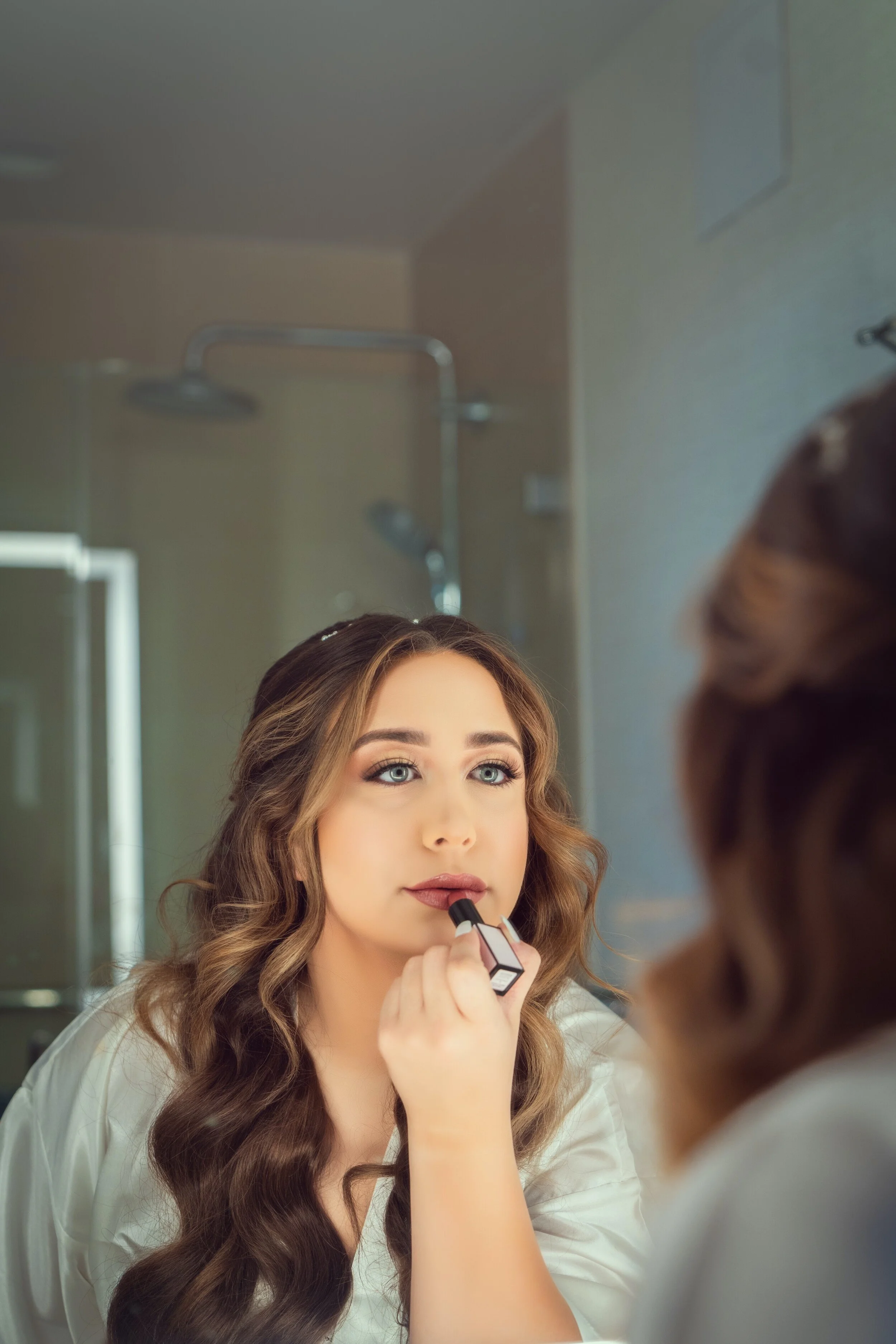 Woman applying lipstick in front of a mirror, focusing on makeup application.