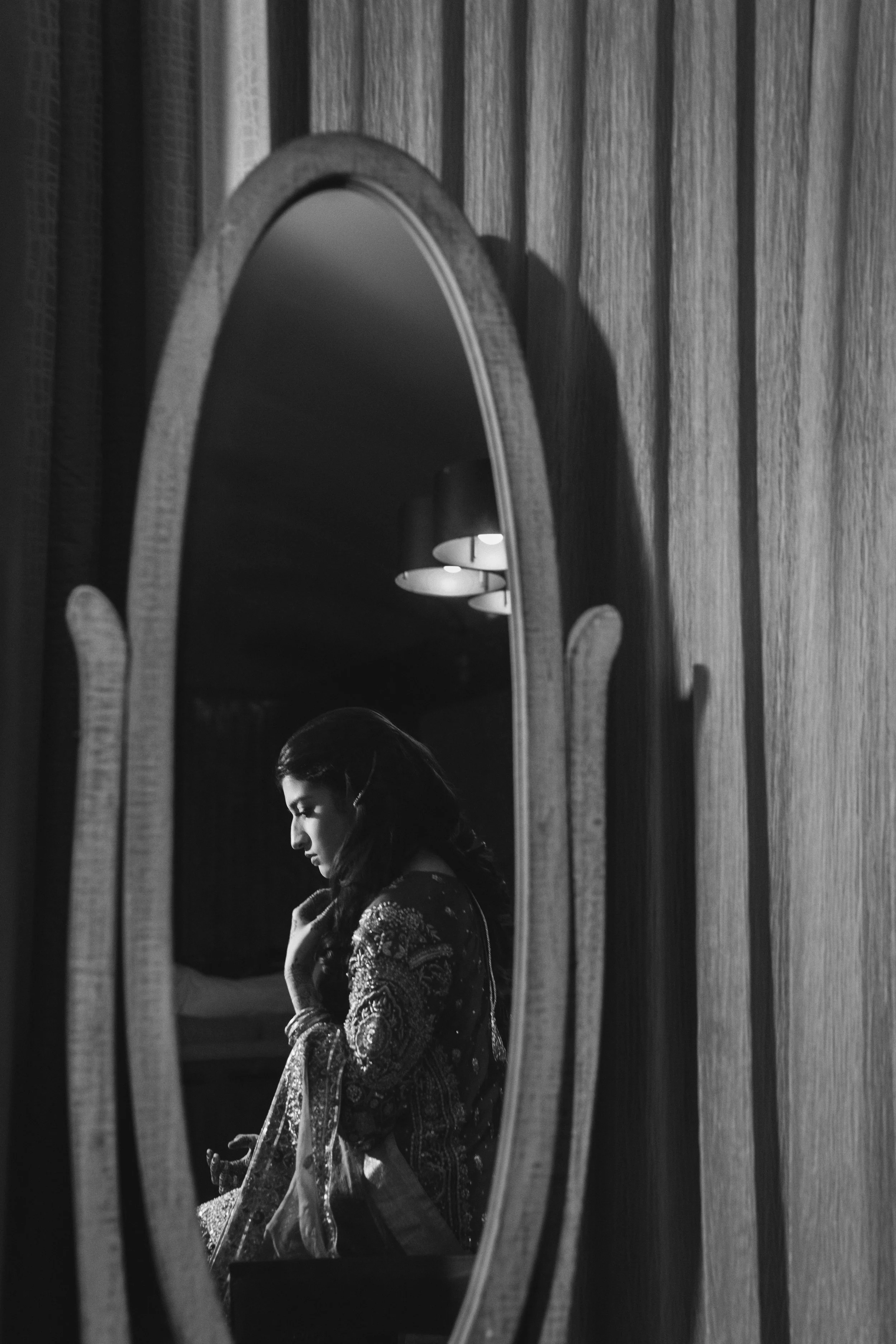 Reflection of a woman in traditional attire in an oval mirror, monochrome.