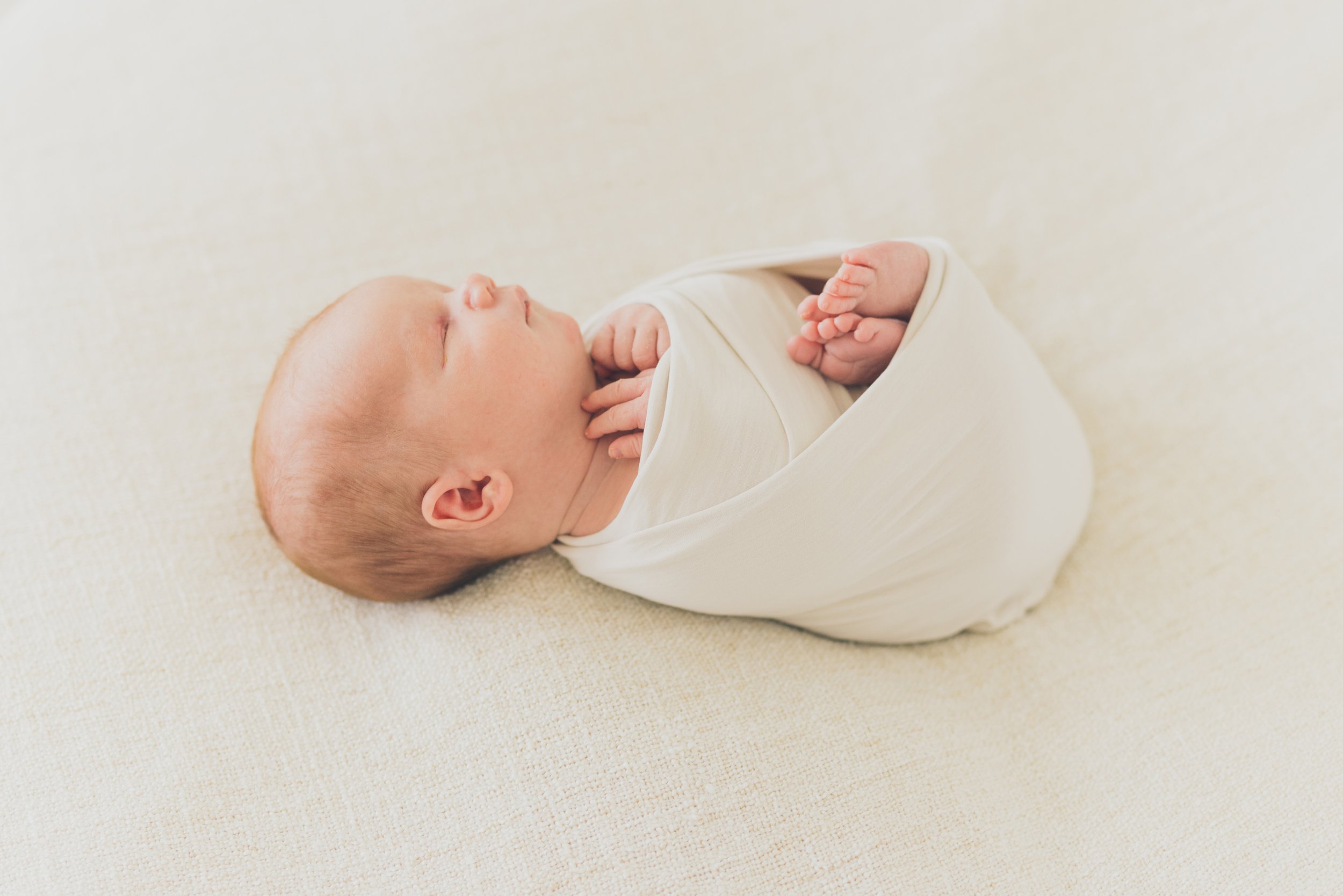  A newborn baby swaddled in a cream wrap in RinkaDink Studio Belfast Northern Ireland. 