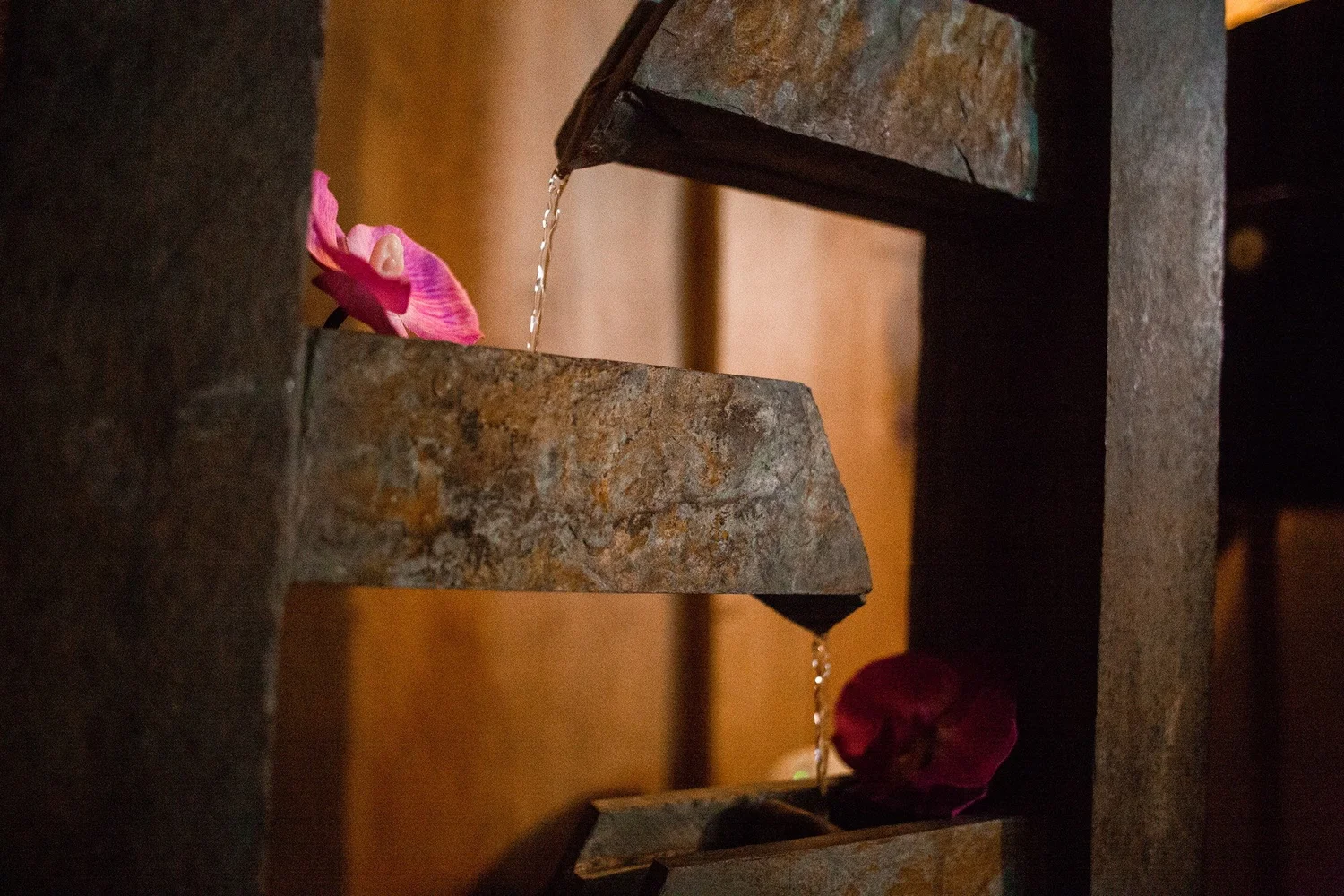 Water trickling down a slate water feature beside pink orchids at Serenity Zen