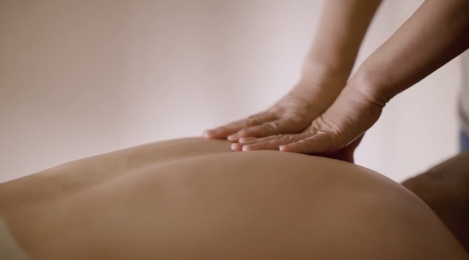 A therapist's hands pressing into a guest's lower back