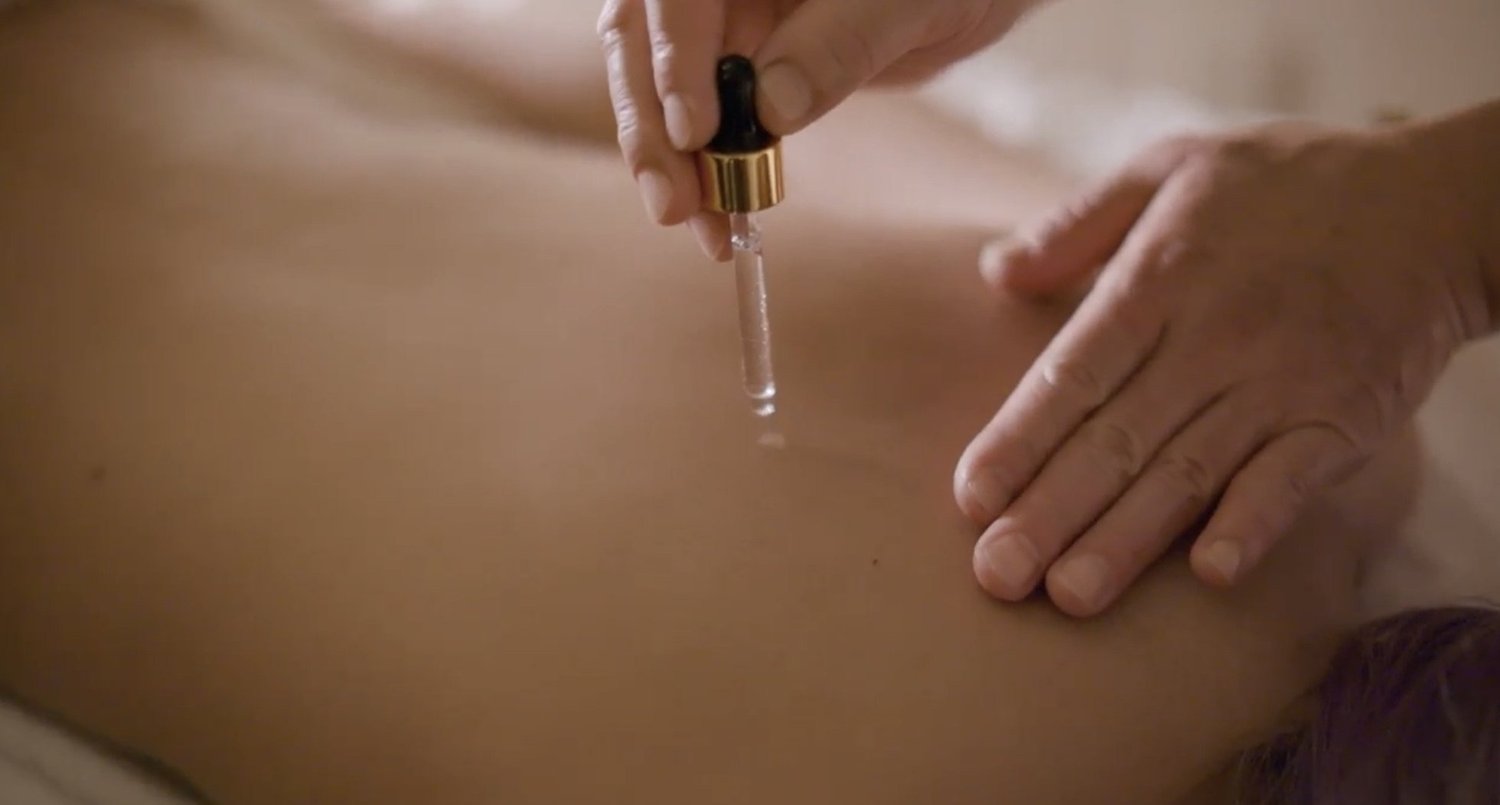 Oil drawn from a dropper onto a guest's back at the start of a body massage