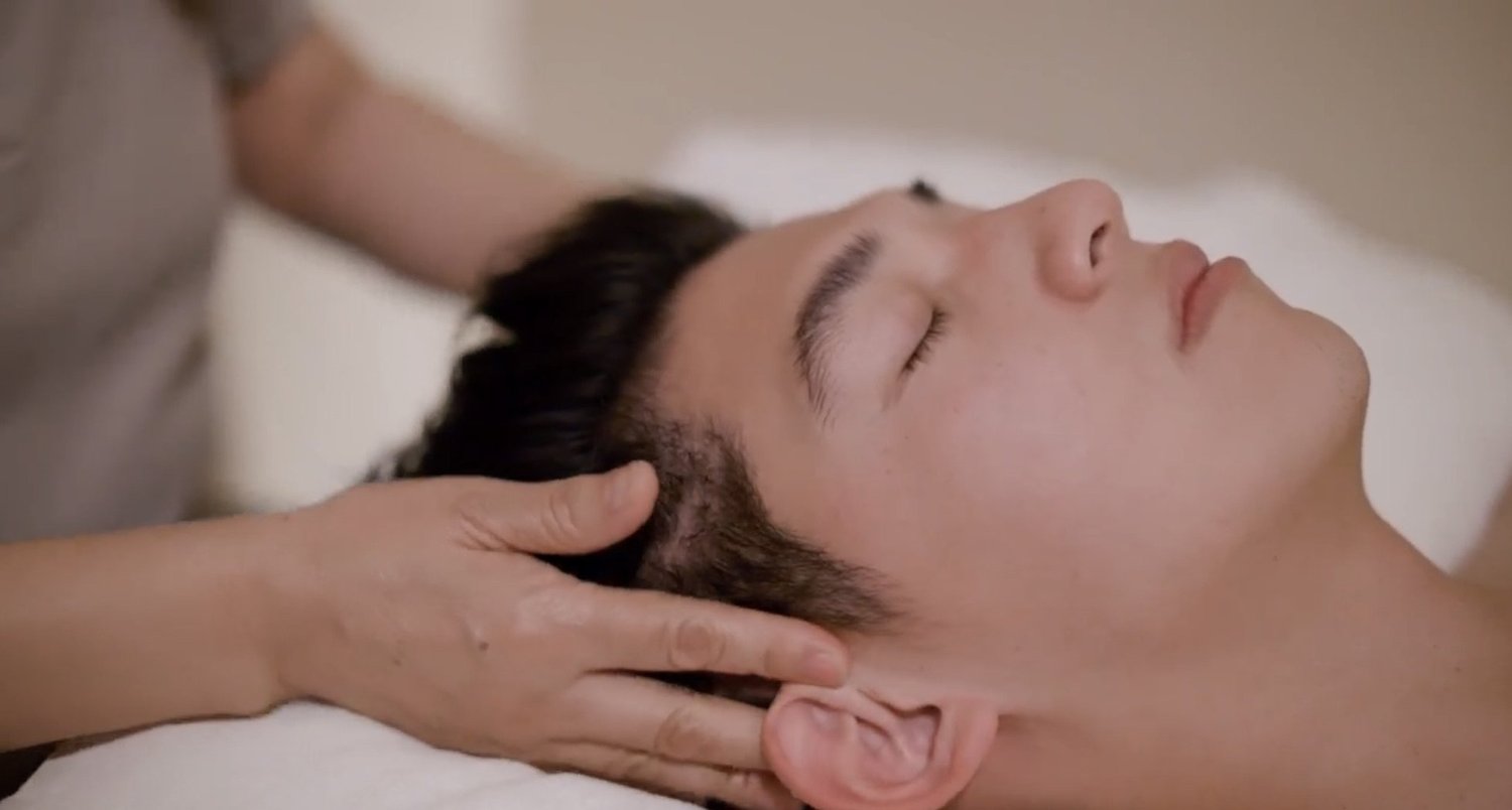 A guest resting with his eyes closed while a therapist's hands work at his temples