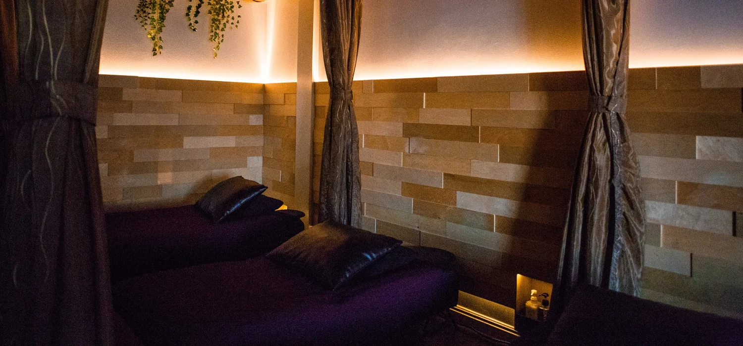 Two curtained stations with plum covers and warm light along the wall in the Reflex Lounge at Serenity Zen in West Covina