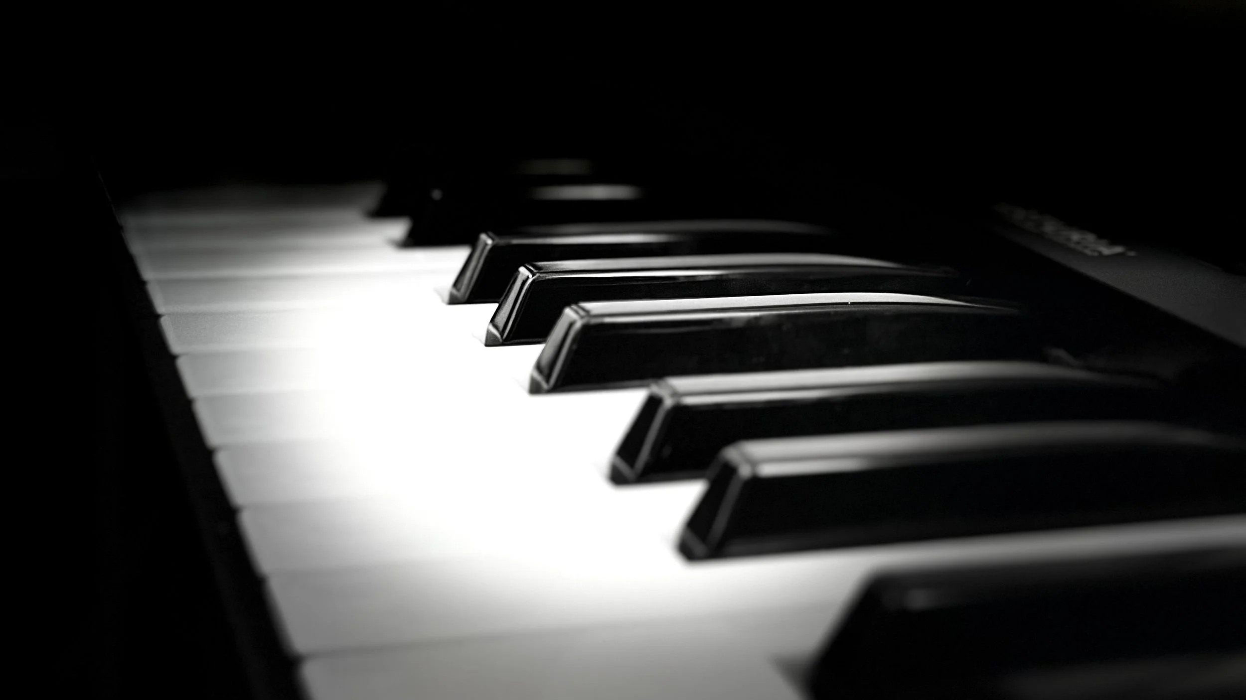 Close-up of piano keys, black and white, in a dimly lit setting.