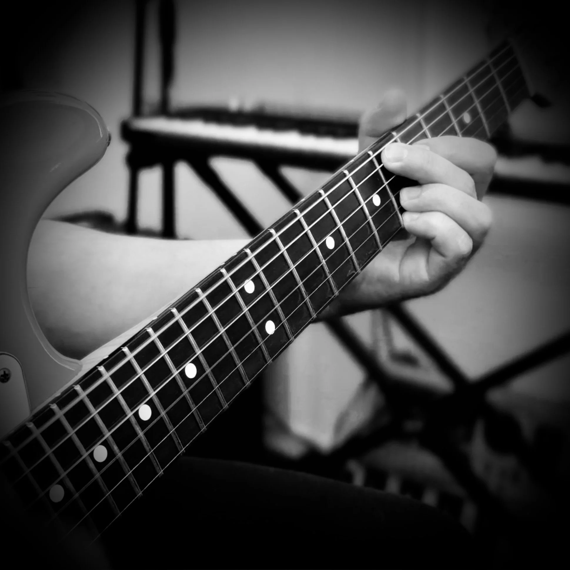 Close-up of a person playing an electric guitar, focusing on their hand on the fretboard, in black and white.