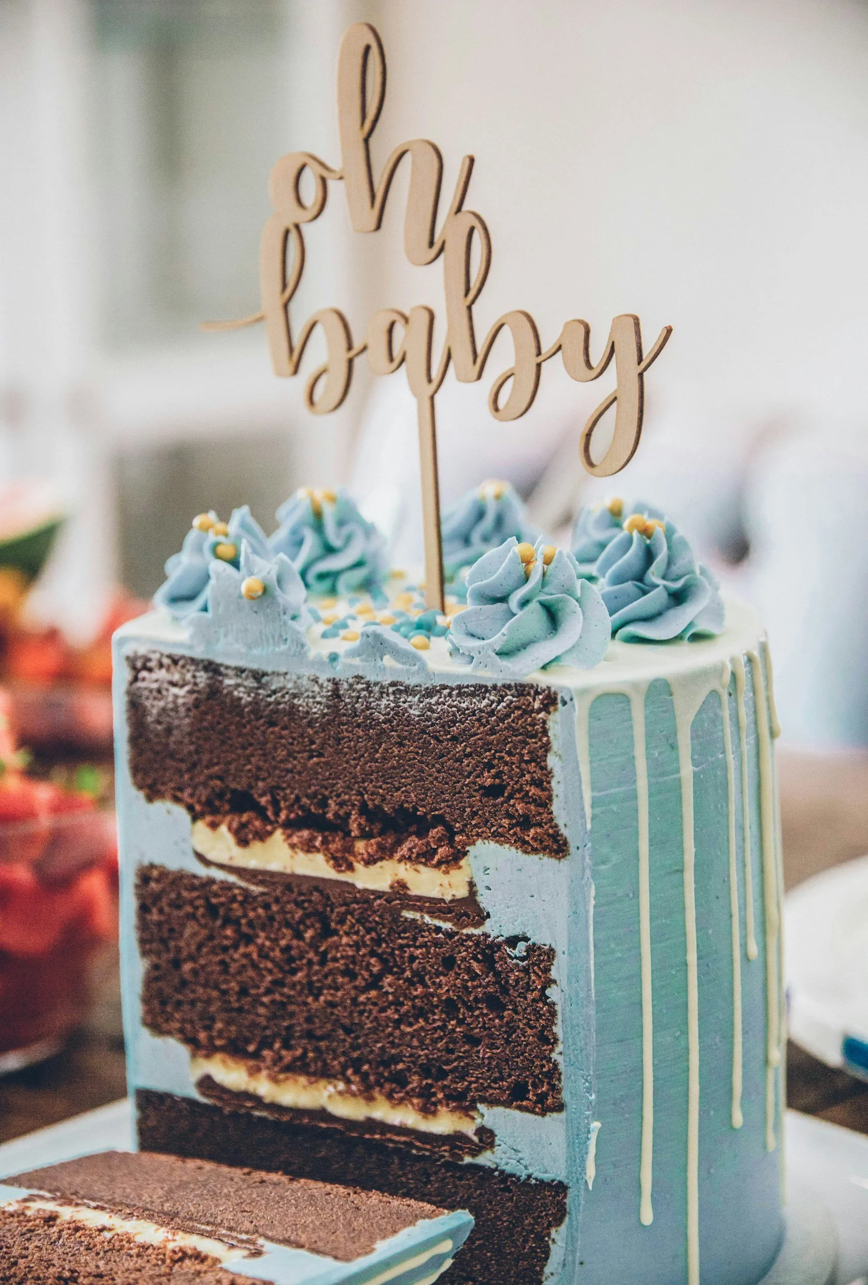 Sliced chocolate layer cake with blue frosting and an oh baby cake topper at a baby shower celebration