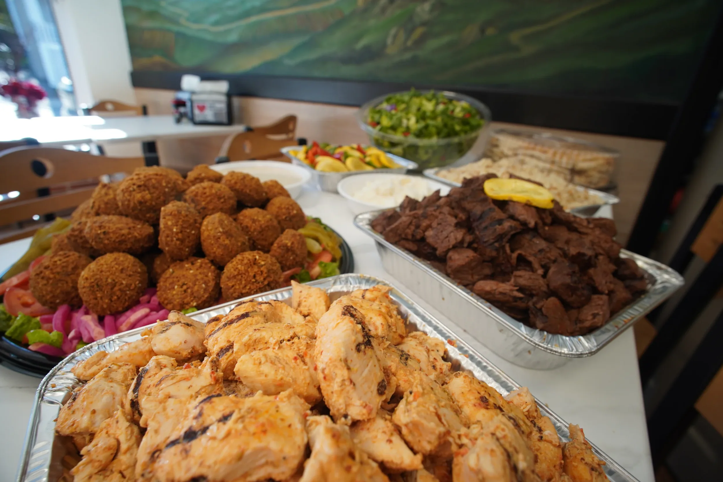 ANI Catering spread showing full catering trays of grilled chicken, beef shawarma, and falafel alongside tabbouleh, pickled vegetables, and flatbread