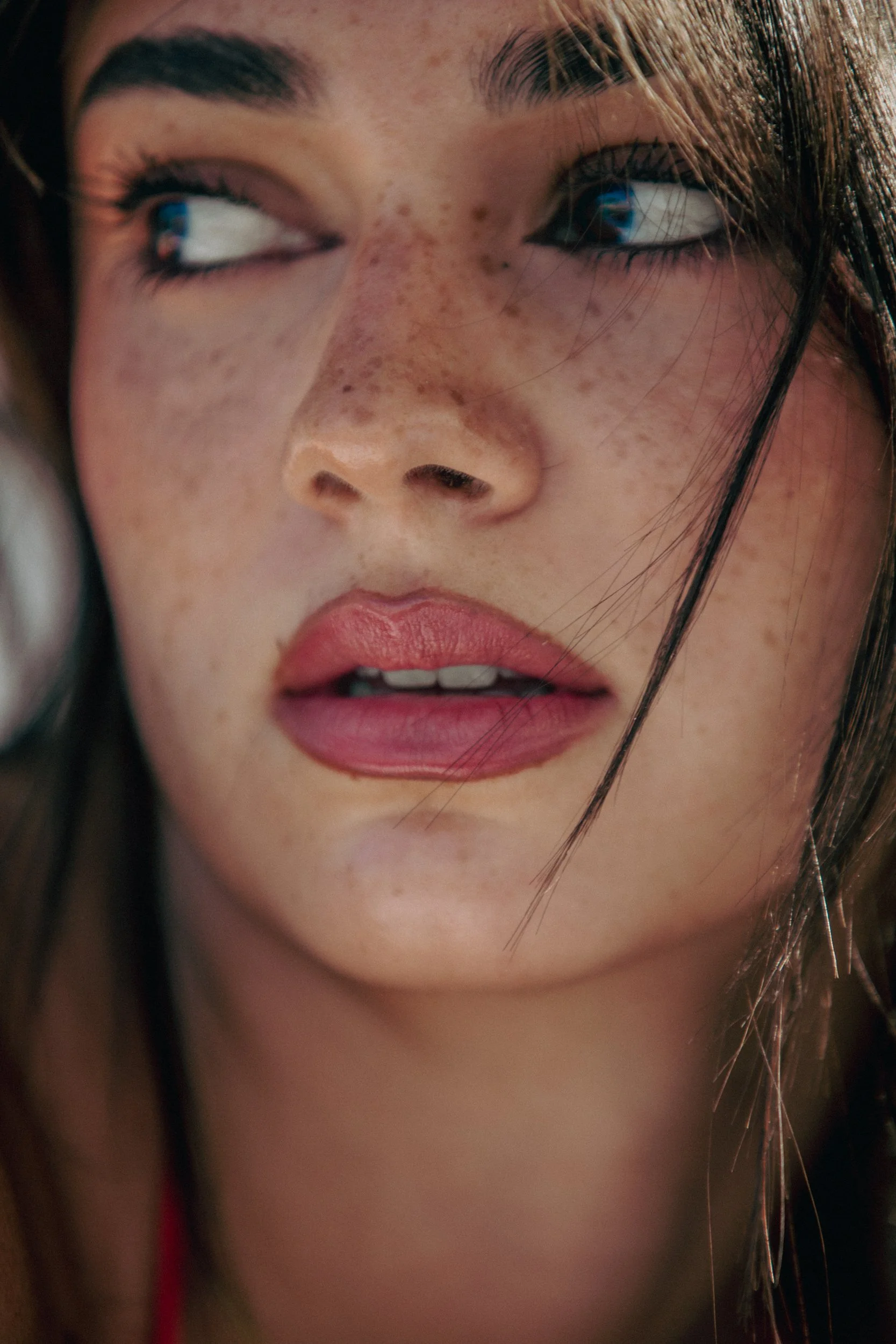 Close-up of a woman's face with dark hair, arched eyebrows, and visible freckles, looking to the side.