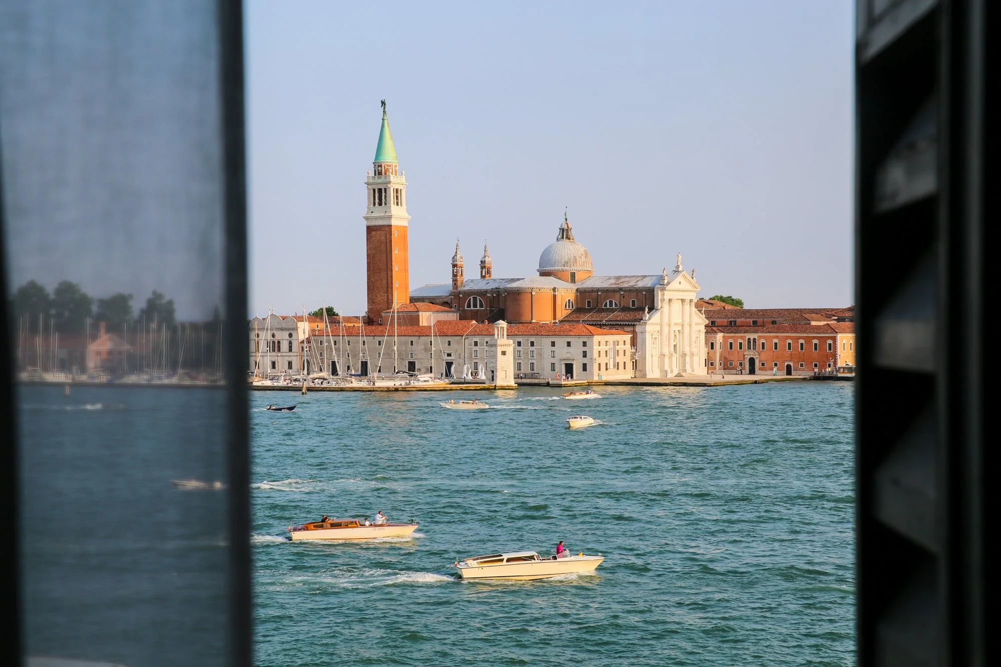 Venice waterfront with boats passing San Giorgio Maggiore church and bell tower across the lagoon