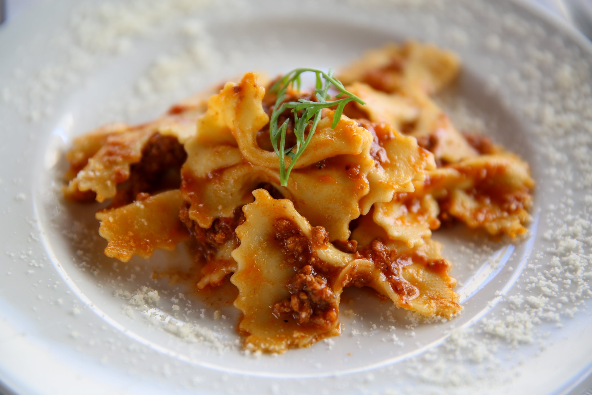 Plate of farfalle pasta with ground meat in tomato sauce, garnished with fresh herbs and grated Parmesan cheese