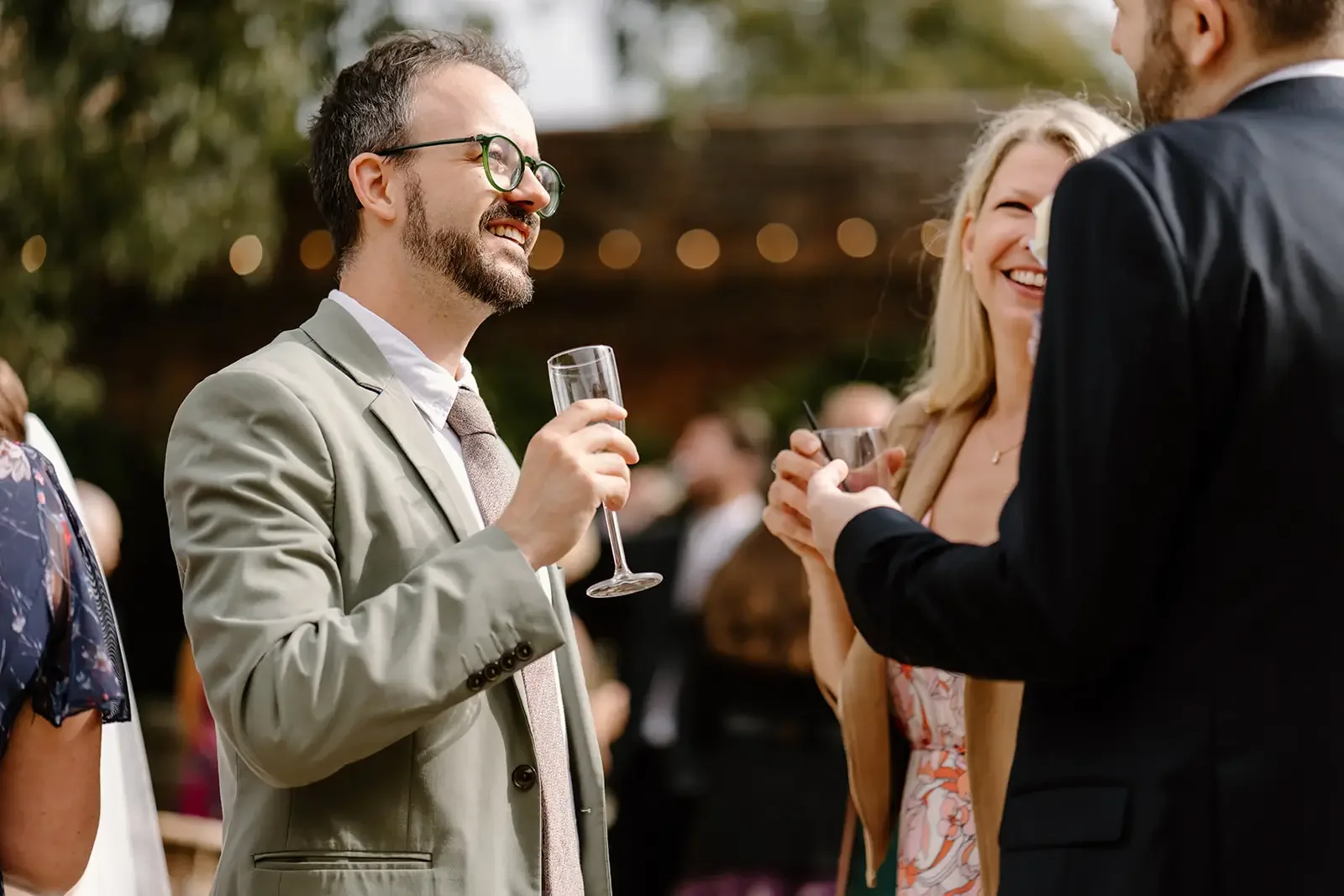 People at an outdoor social gathering holding drinks and chatting, with smiling faces.