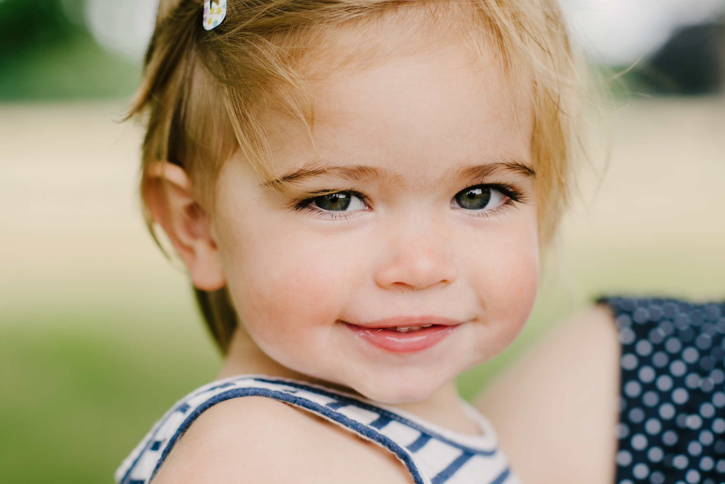 close up of a little girl being held by mummy smiling to camera in the park | Children's Photographer Aylesbury Buckinghamshire and Thame Oxfordshire
