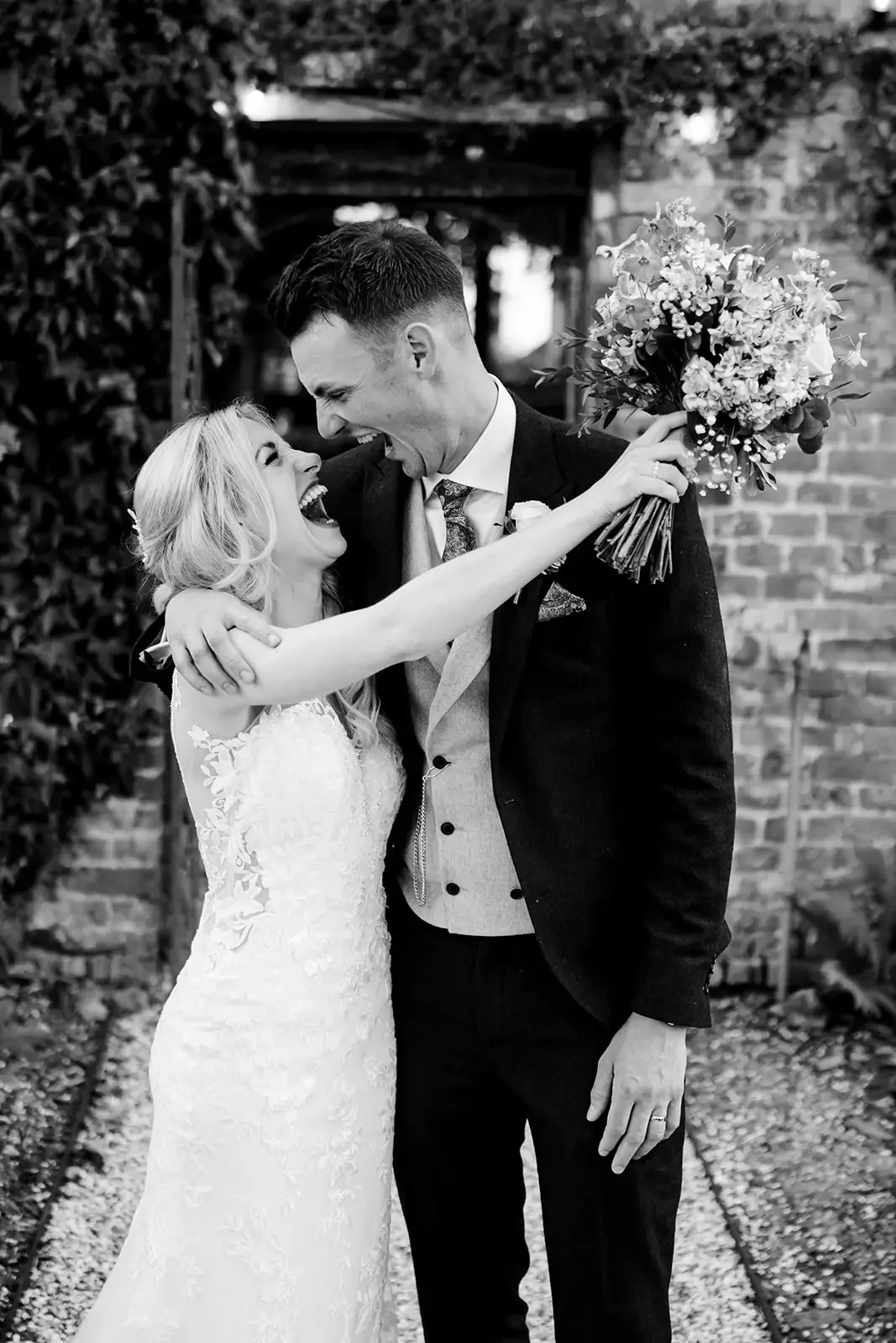 A joyful bride and groom celebrate outdoors, with the bride holding a bouquet of flowers and both sharing a happy moment.