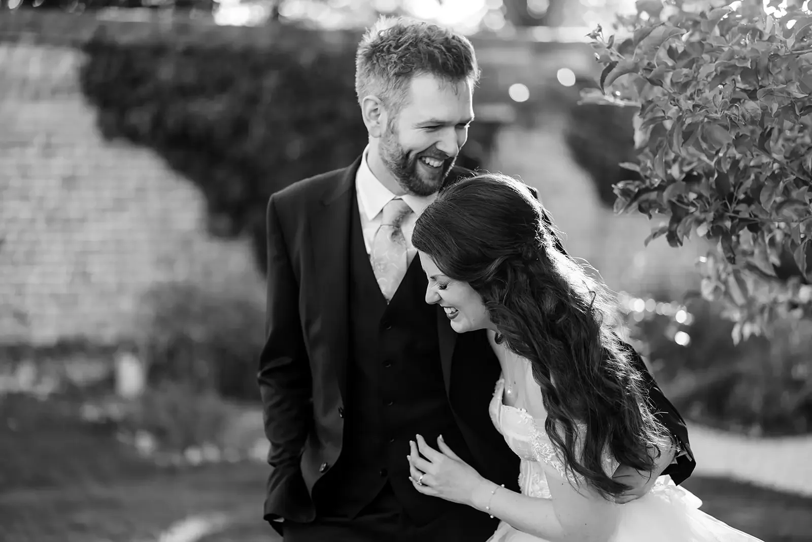 A black and white photo of a couple laughing and enjoying each other's company outdoors, with trees and blurred background.