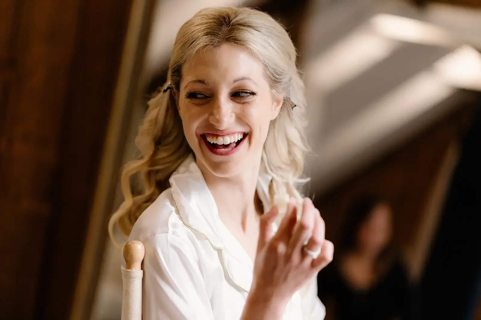 A woman with blonde hair smiling and looking to the side, indoors.