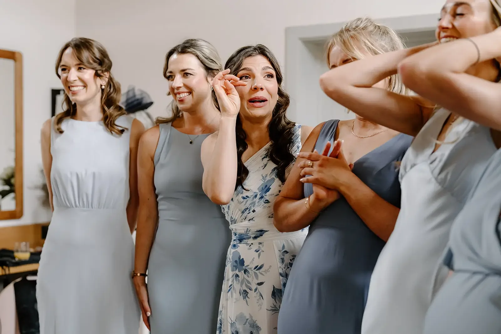 Group of women in formal attire, some smiling and one woman crying, in an indoor setting.