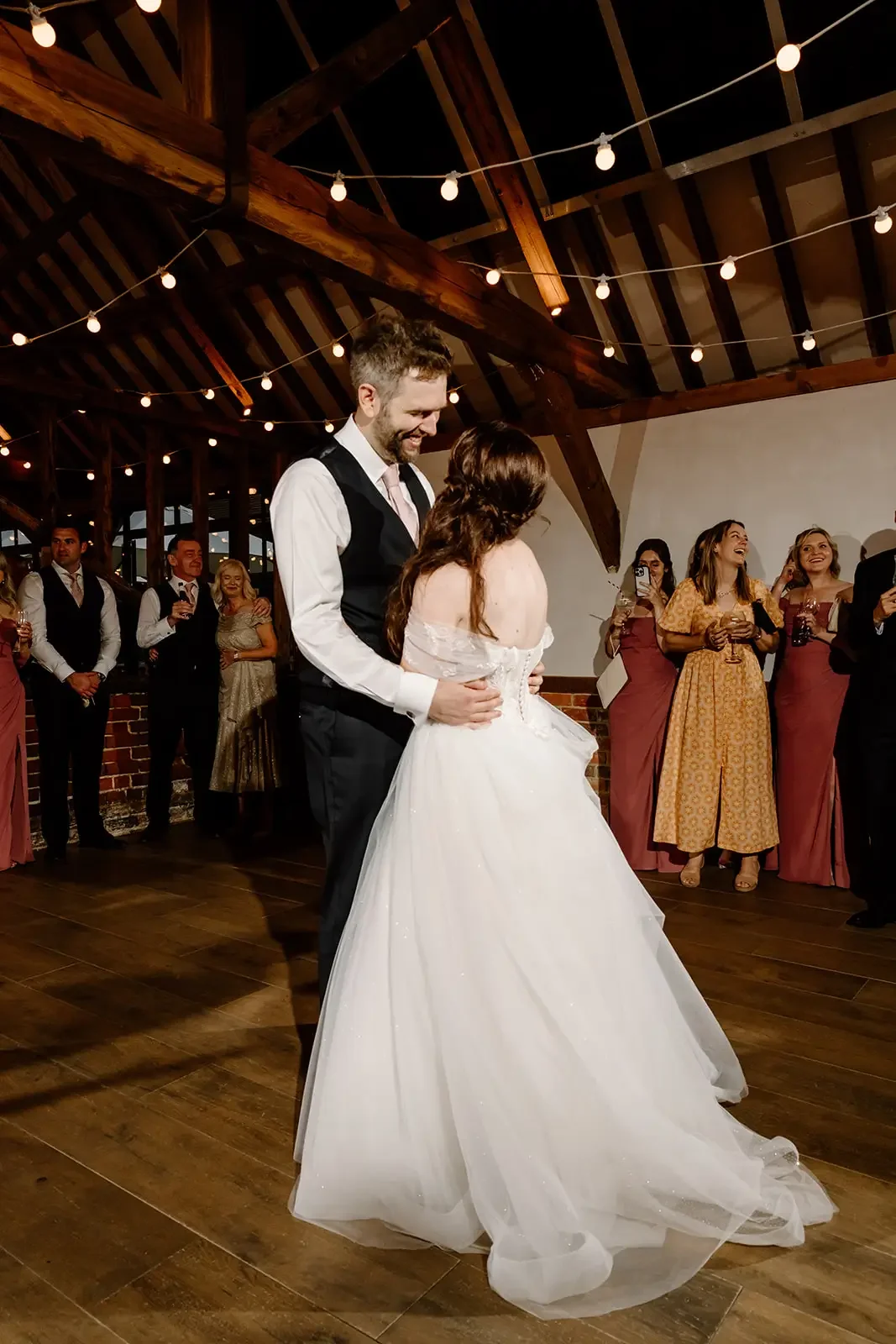 Bride and groom dancing at their wedding reception with guests watching and smiling in the background.