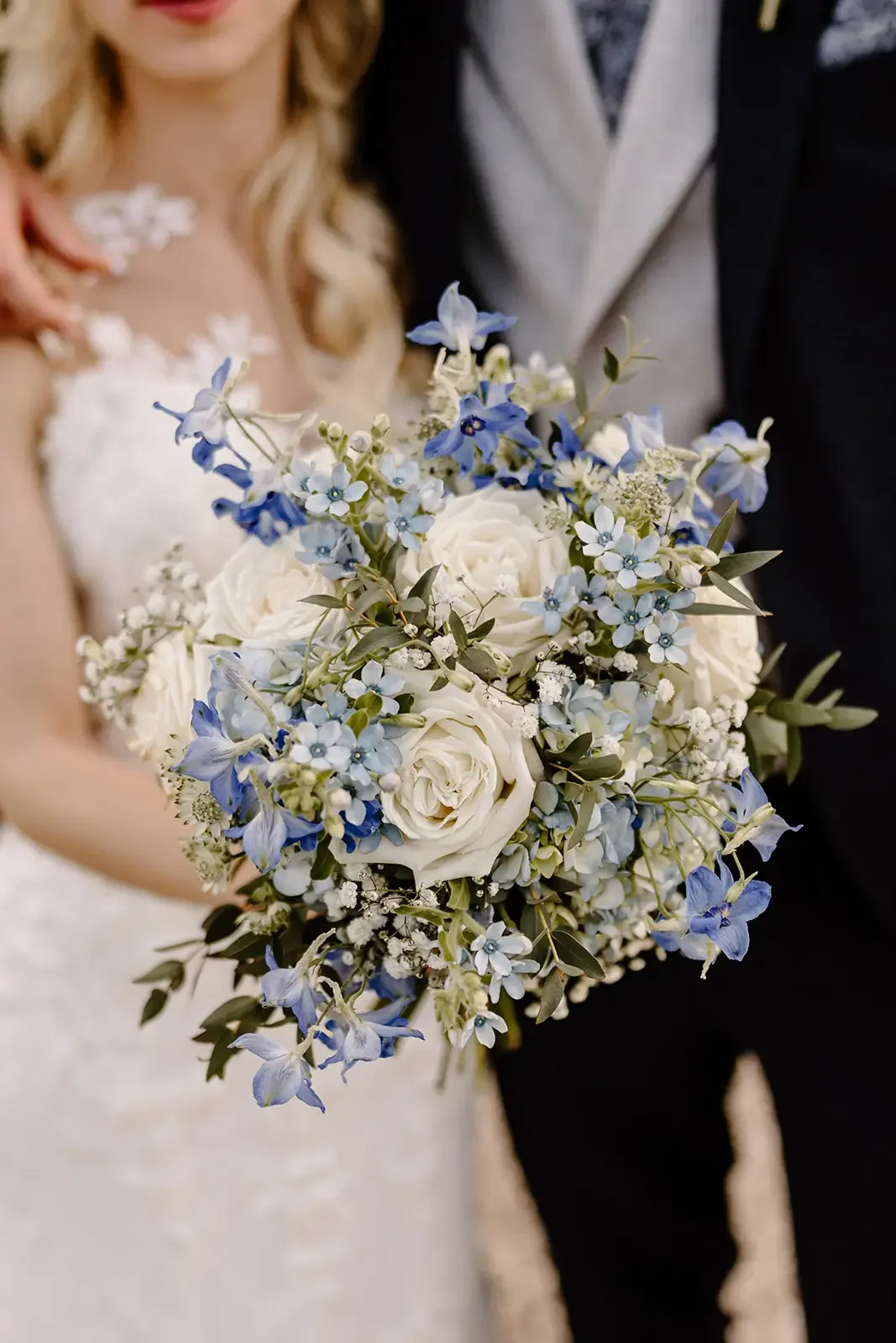 Bride holding a bouquet of white and blue flowers during a wedding.