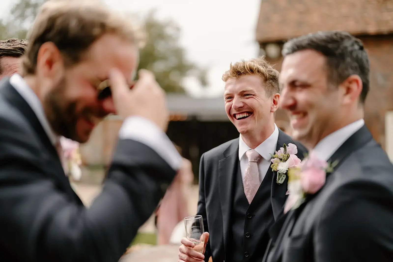 Grooms in suits sharing a laugh at a wedding celebration outside.