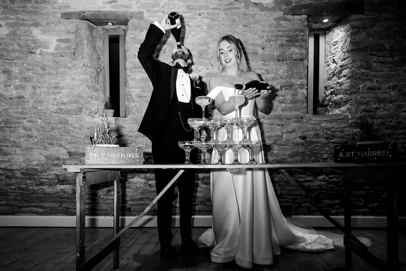 Bride and groom in wedding attire pouring champagne into a pyramid of glasses at their wedding reception.