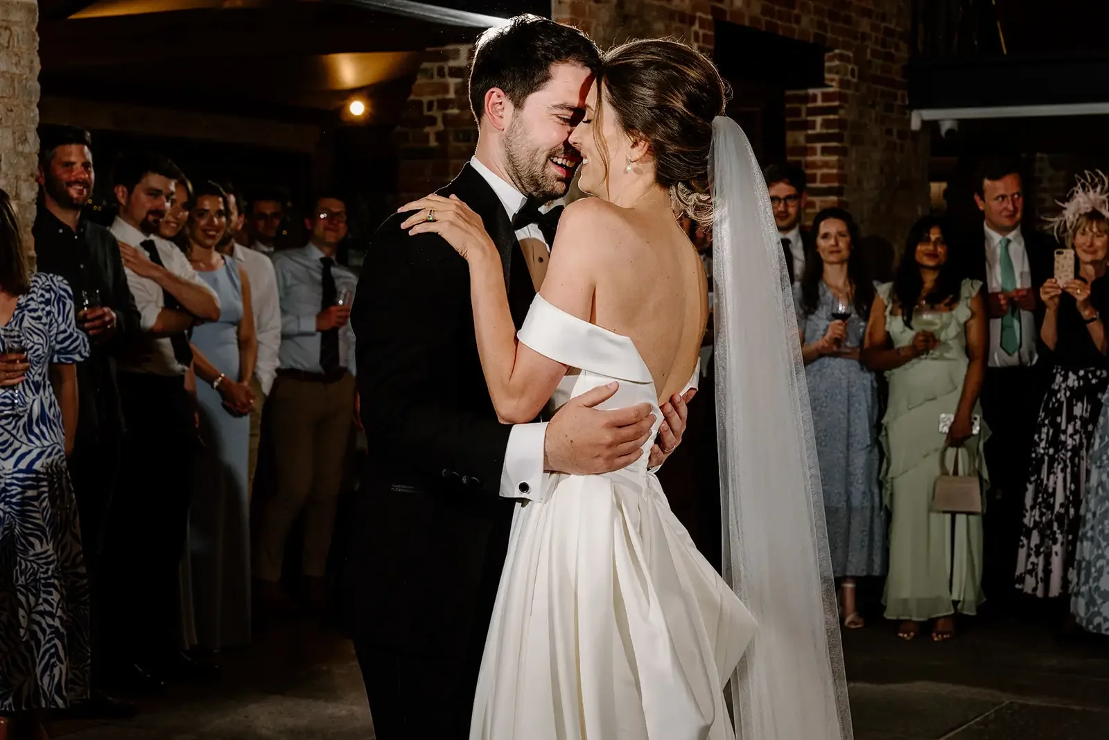 Bride and groom dancing at their wedding, surrounded by guests watching and smiling.