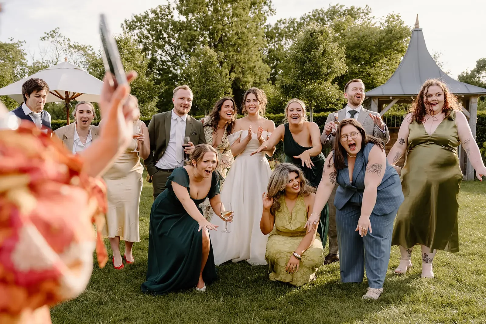 Group of people celebrating outdoors at a wedding reception with greenery and a gazebo in the background