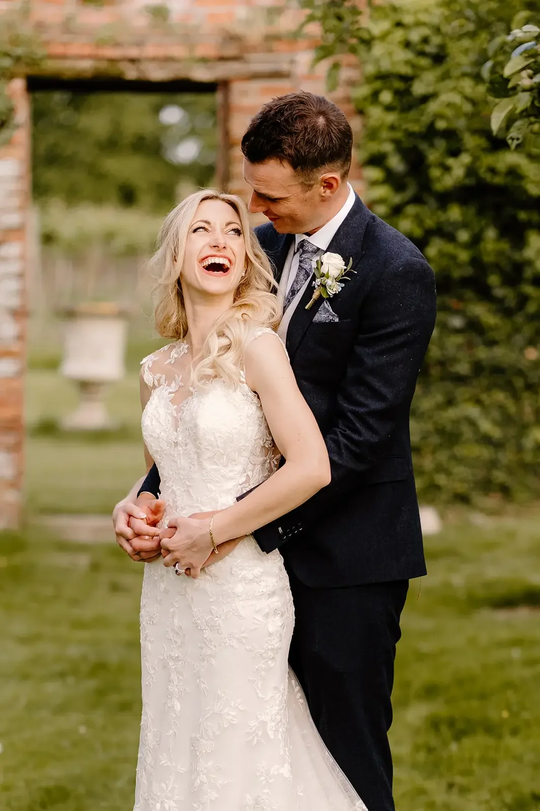A happy bride and groom sharing a joyful moment outdoors on their wedding day, with the groom holding the bride close and both smiling.