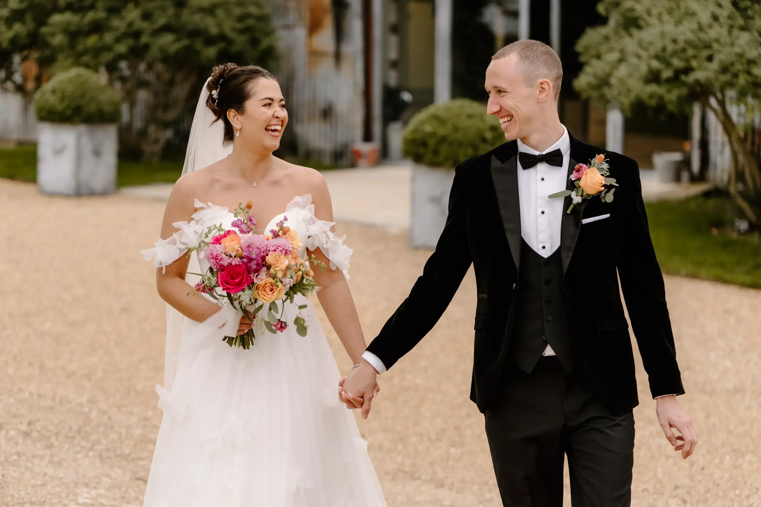 A bride and groom walking hand in hand, smiling at each other, during their wedding celebration outside.