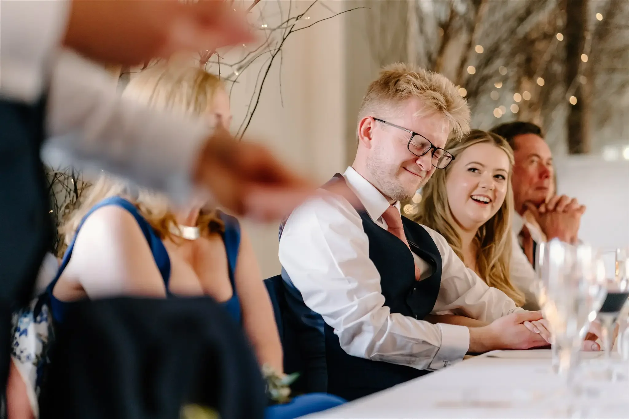 A group of people sitting at a long table during a celebration or special event, with some smiling and others observing.