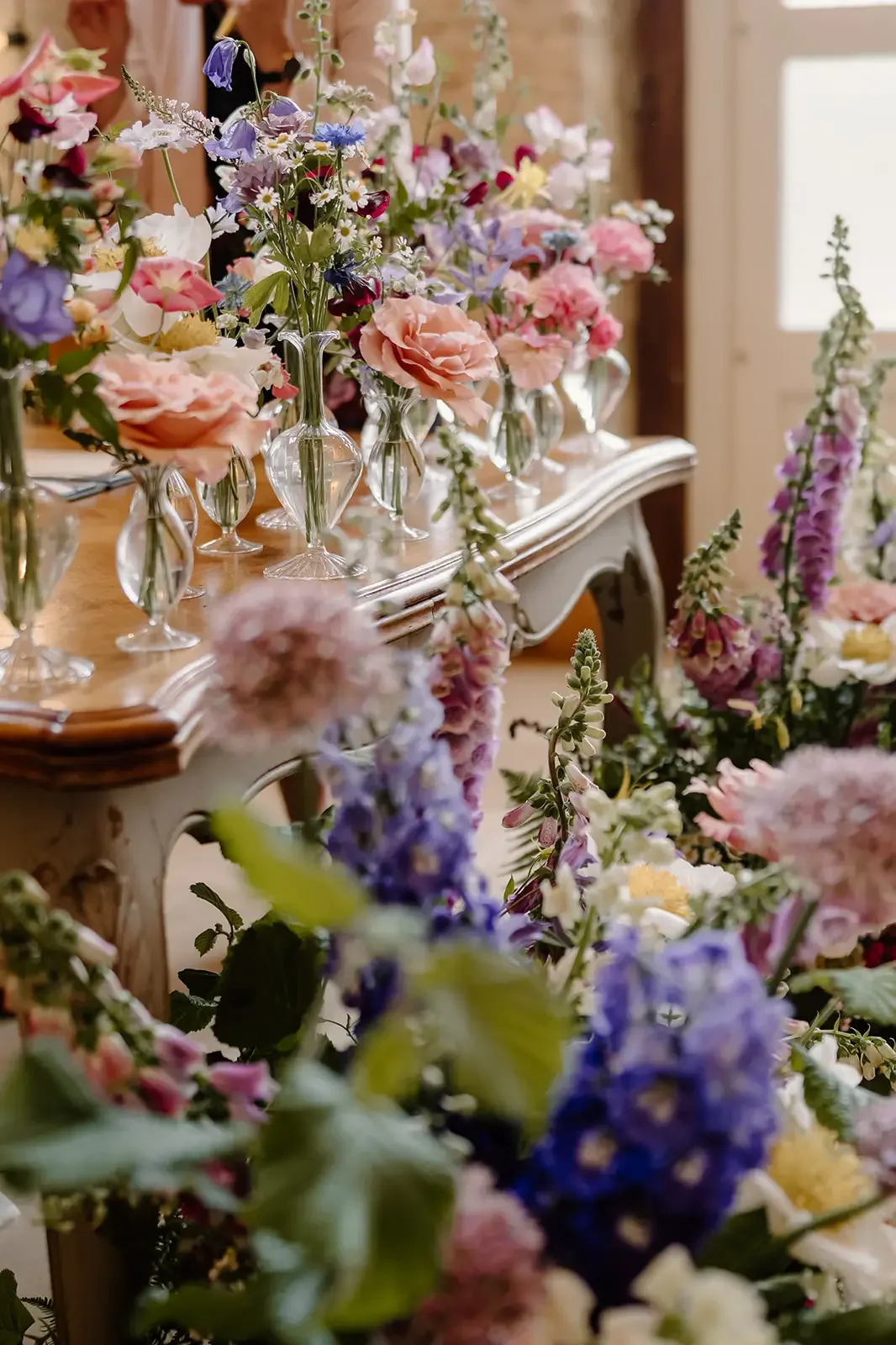 Various colorful flowers arranged in glass vases on a vintage-style table in a well-lit room.