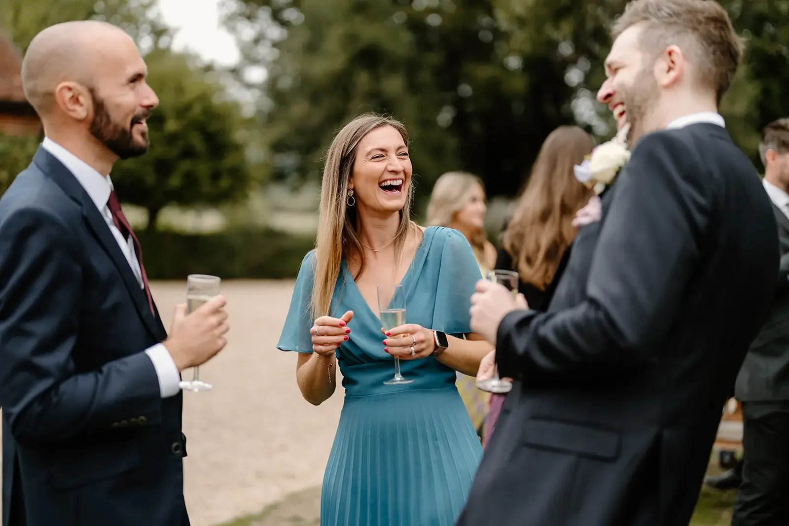 People at a wedding reception talking and laughing outdoors, holding glasses of champagne.