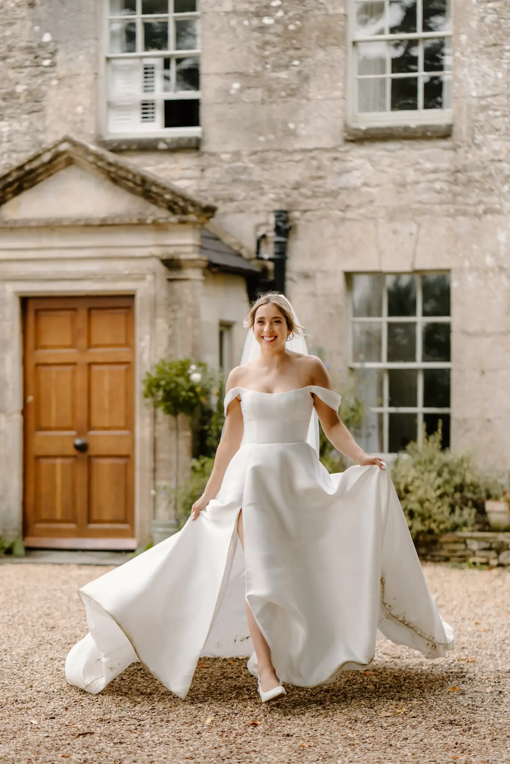 A bride in a white wedding dress walking outdoors with a historic stone building in the background.