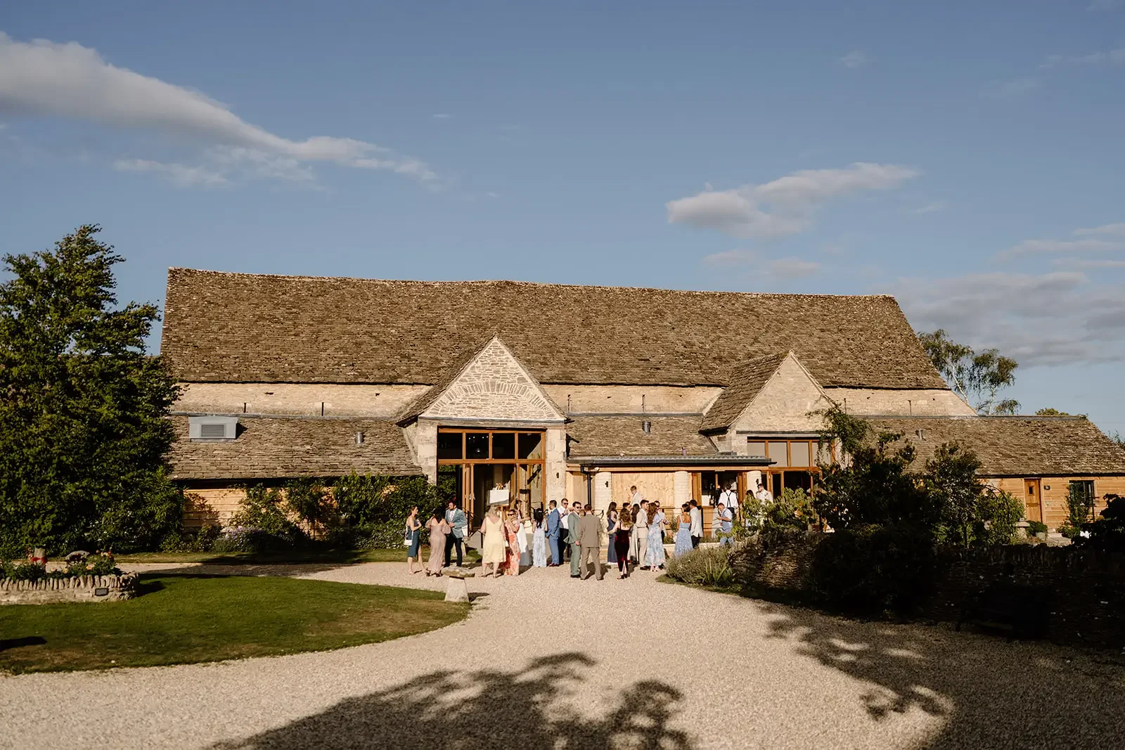People gathered outside a rustic barn on a farm during a sunny day with partly cloudy sky.