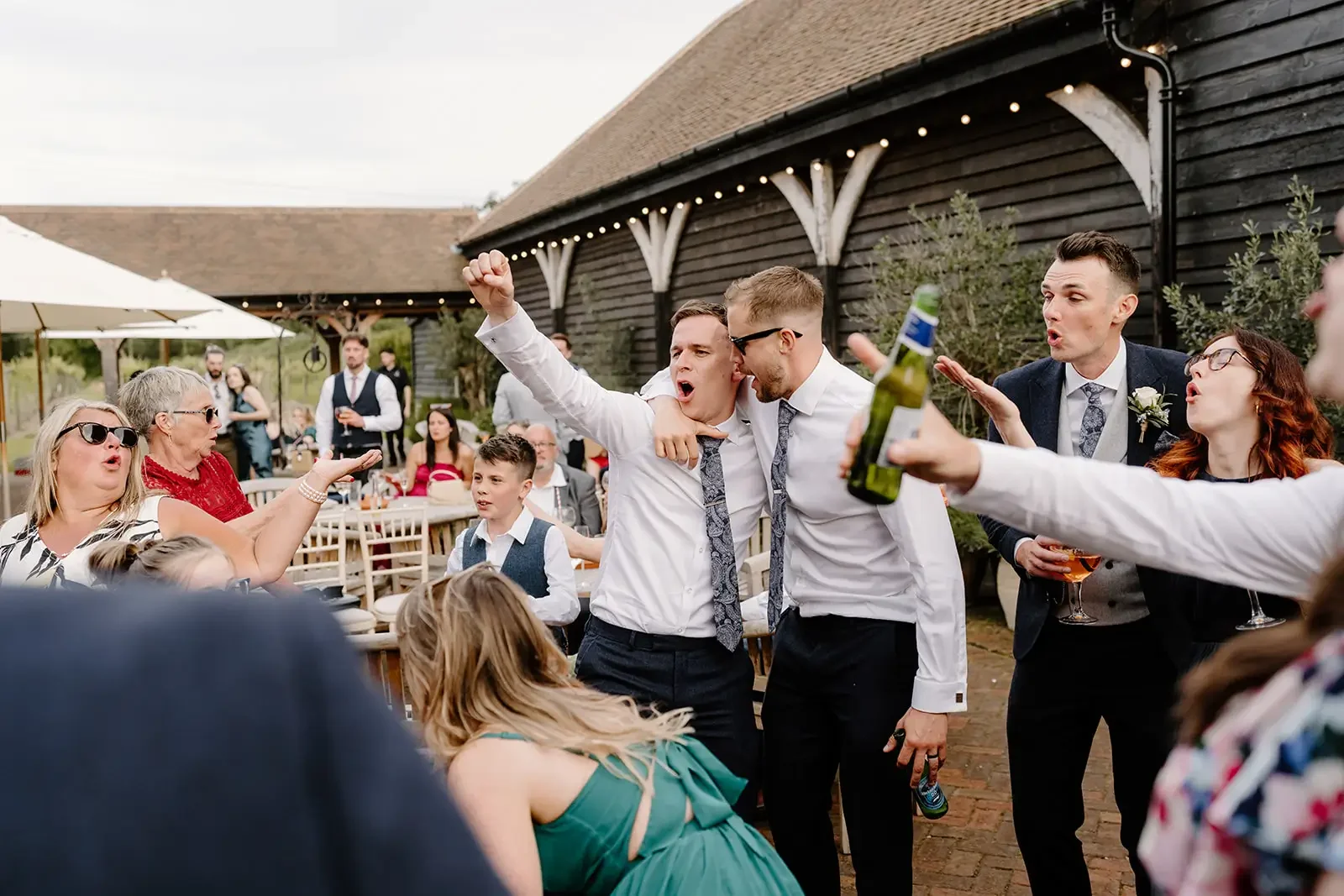 Group of people celebrating at a wedding reception outdoors, singing and dancing.