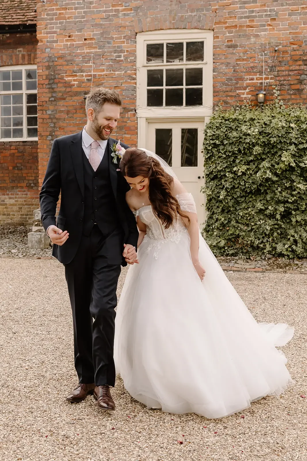 A bride and groom walking hand in hand outside in front of a brick building, sharing a joyful moment.