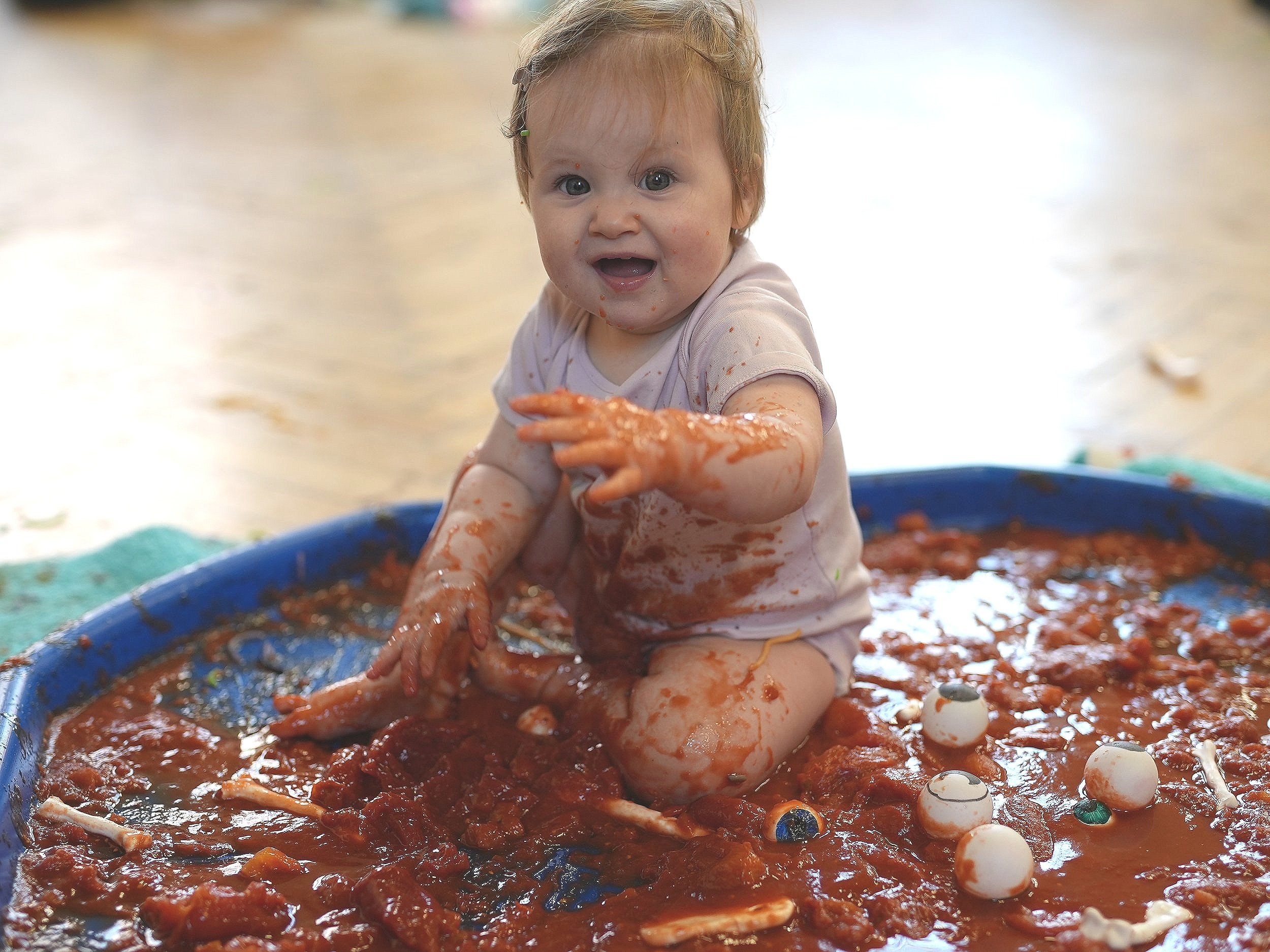  Little girl sitting and playing in a huge tuff tray of tinned tomatoes and bones and eyes 