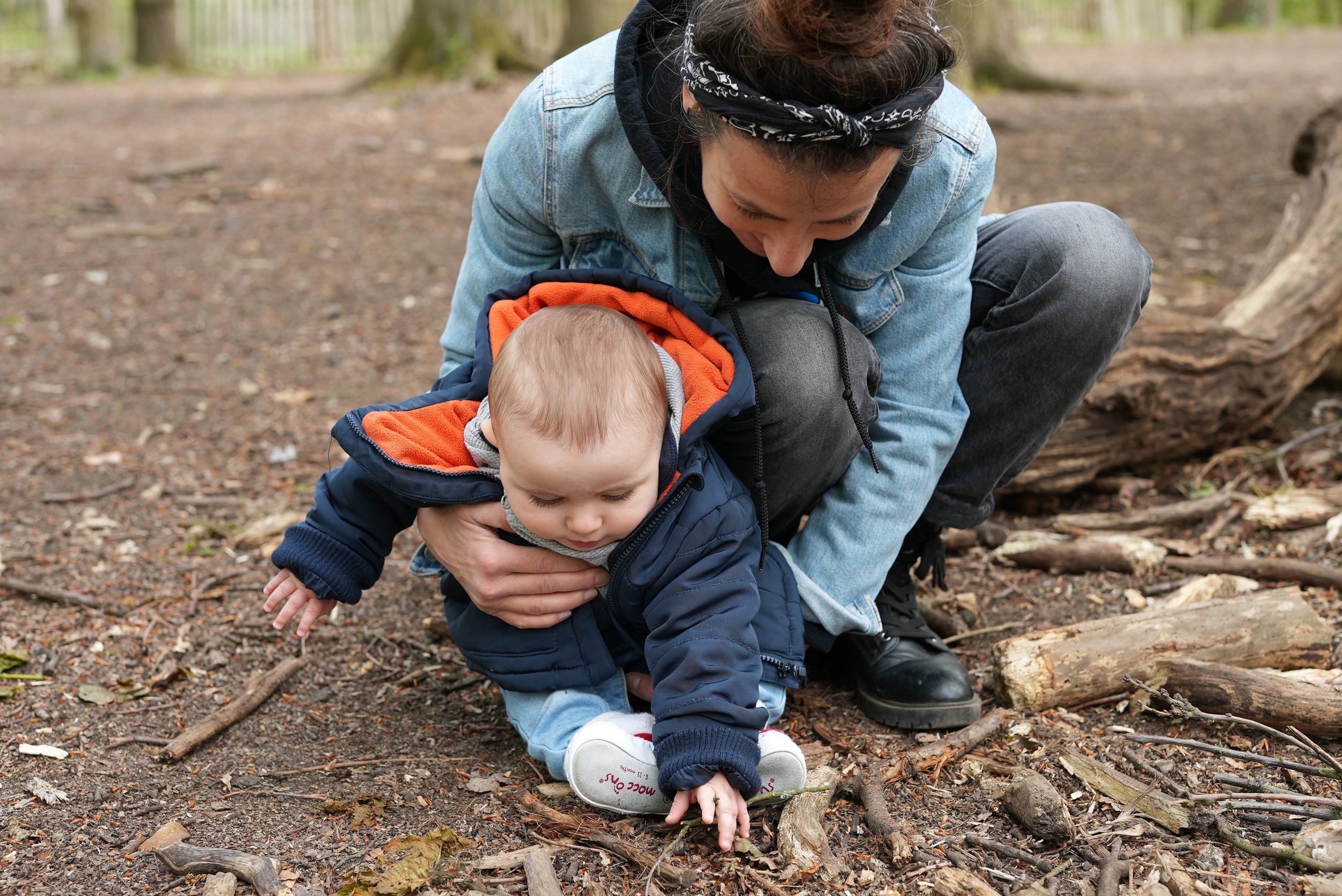  Mum is holding her little one and letting him pick things up from the ground. They are enjoying a woodlands session 