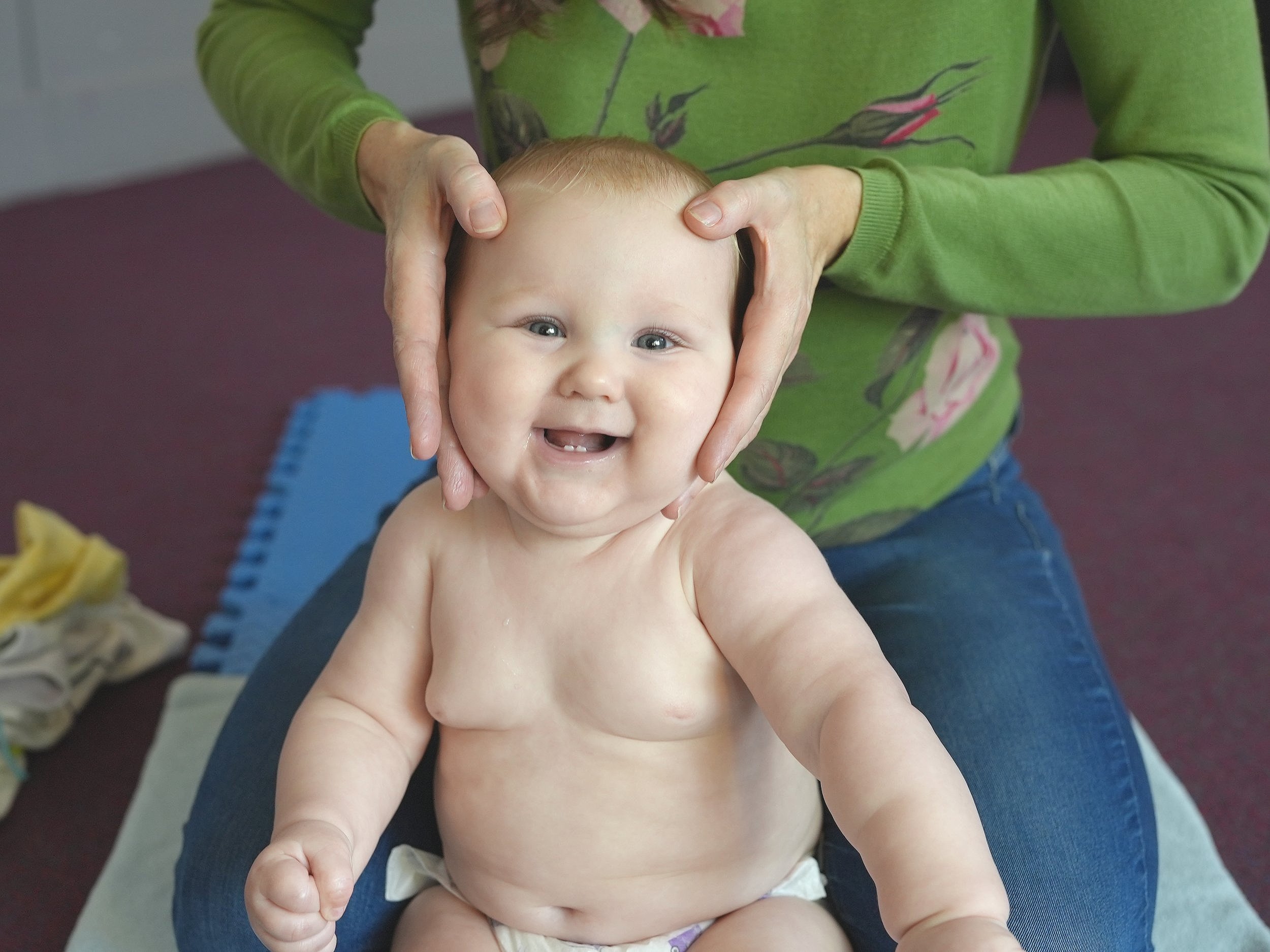  Baby is getting a head massage whilst sitting up. She has a huge smile on her face and seems to be enjoying this stroke 