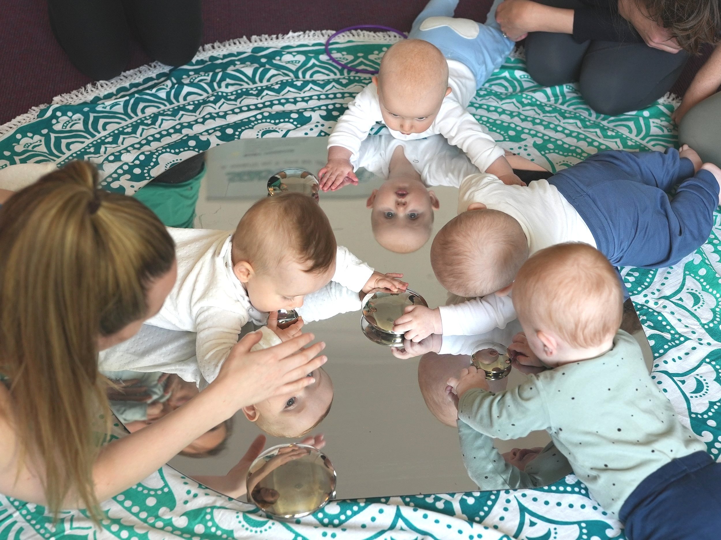  4 babies are laying on a mirror looking at themselves  