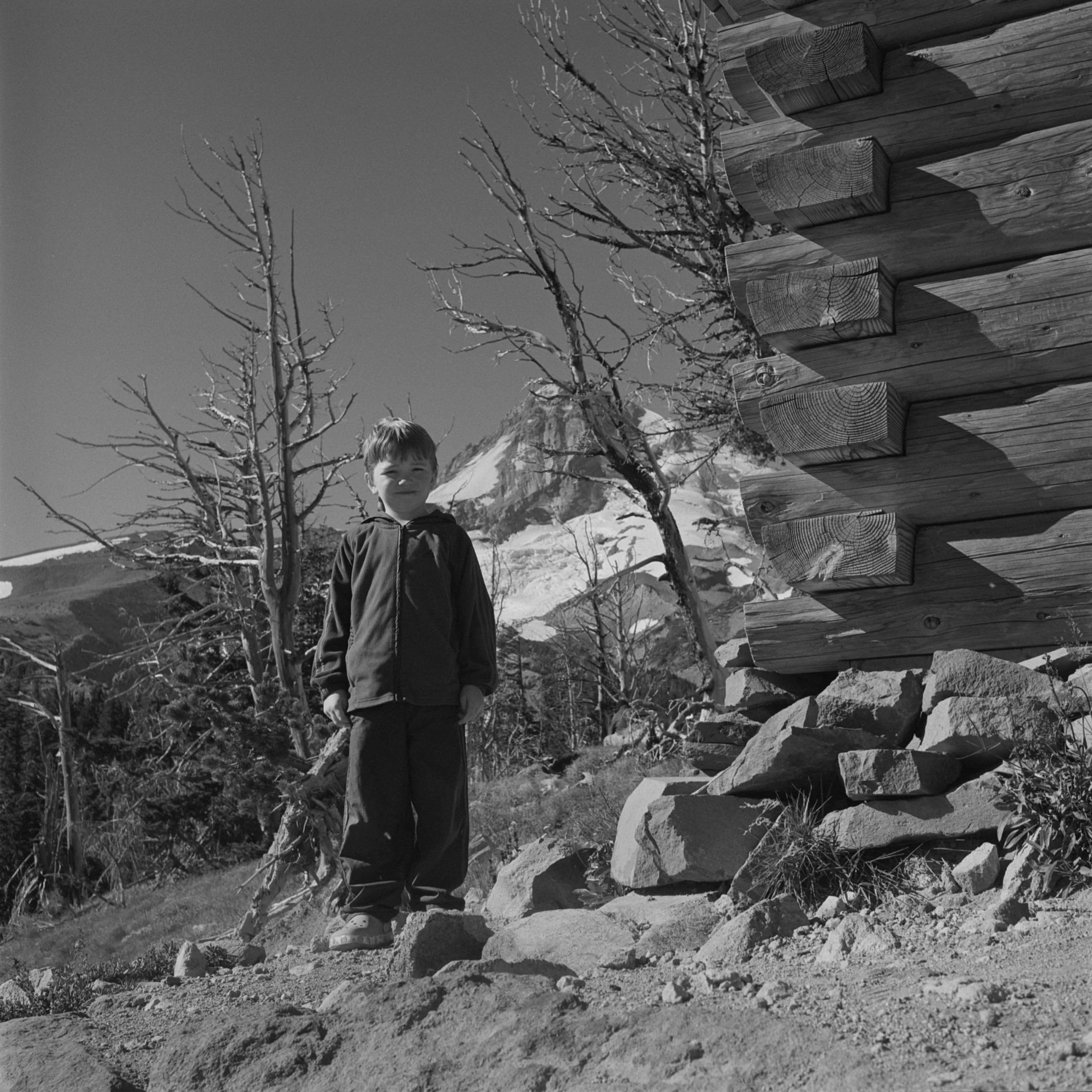 My son George standing next to the notched log corner and stone foundation of Cloud Cap Inn's guest wing.